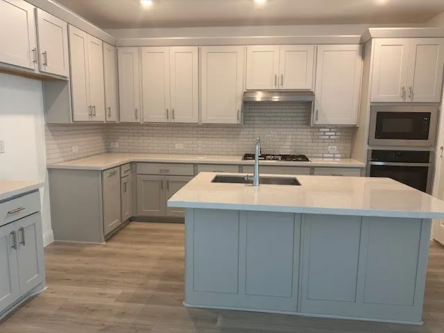 Kitchen featuring light gray cabinetry, light-toned countertops, a subway tile backsplash, stainless steel appliances, and wood-finish flooring