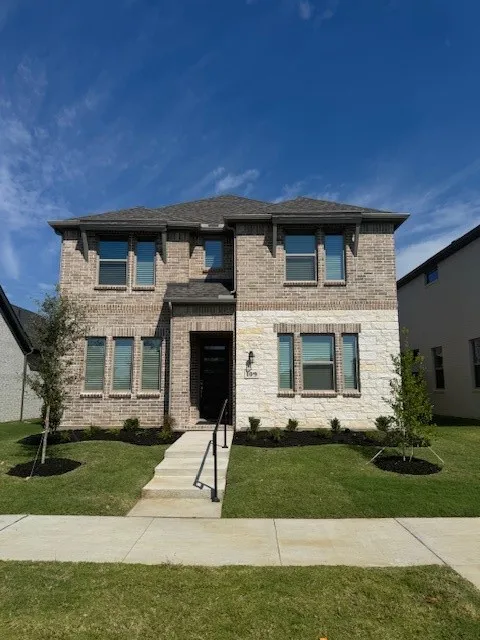 Two-story exterior featuring brick and stone cladding, multiple windows, a prominent entry, and a manicured lawn