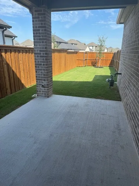 Covered patio with brick column, concrete flooring, and an expansive lawn area