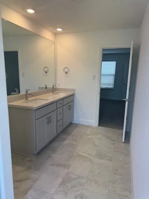 Spacious bathroom featuring a double vanity with grey cabinetry, stone-finish countertop, dual undermount sinks, and an expansive wall-mounted mirror