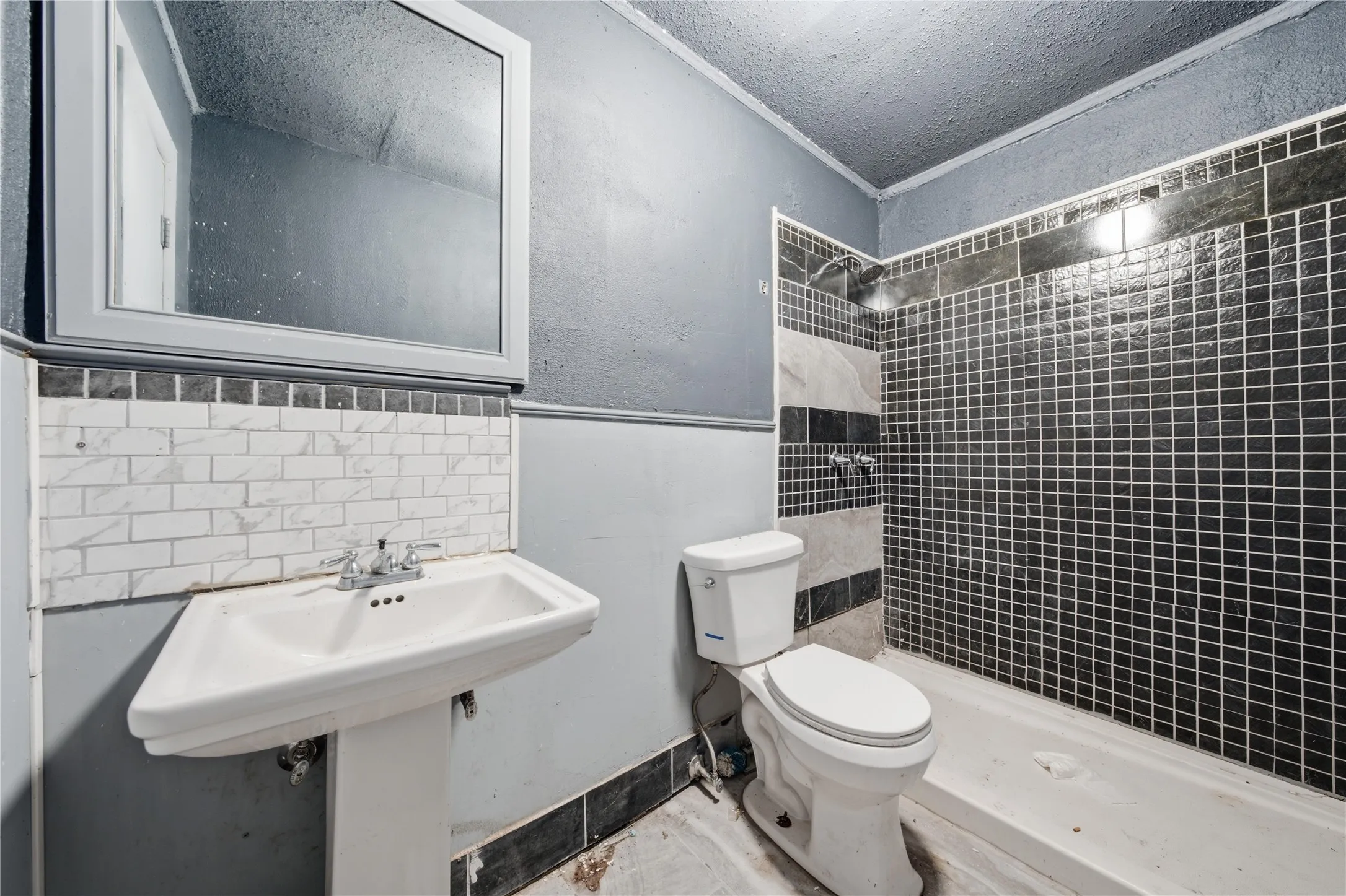 Pedestal sink, wall-mounted mirror, and tiled shower surround