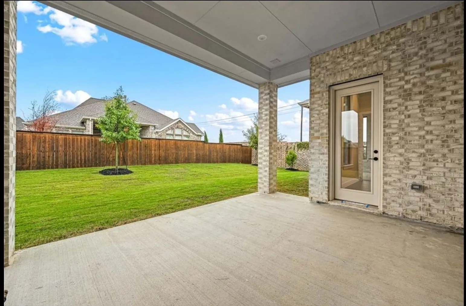 Covered patio with a concrete surface, light-toned brick exterior, and a full-light glass door
