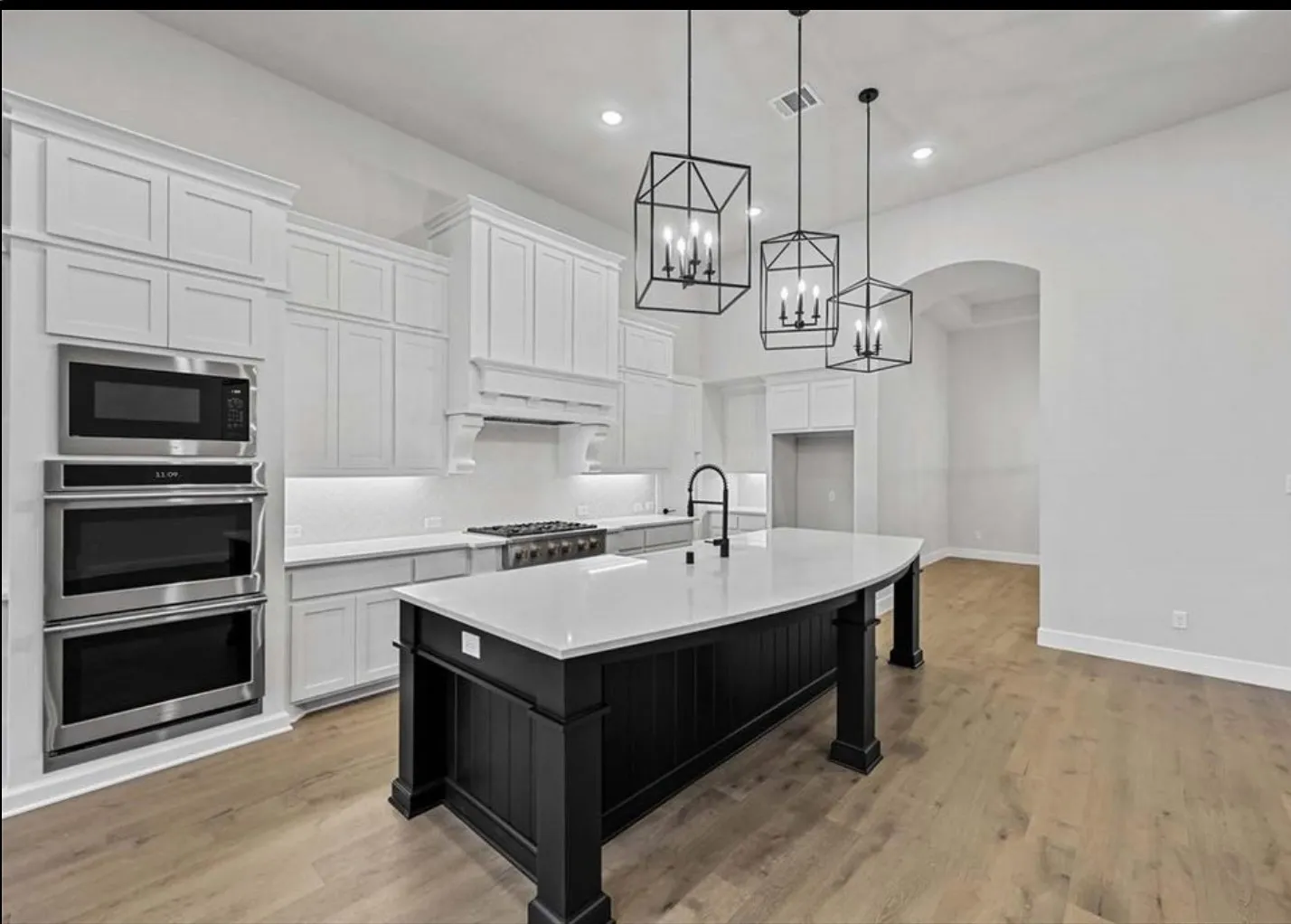 Gourmet kitchen featuring a curved island with white countertop, white shaker-style cabinetry, and stainless steel appliances