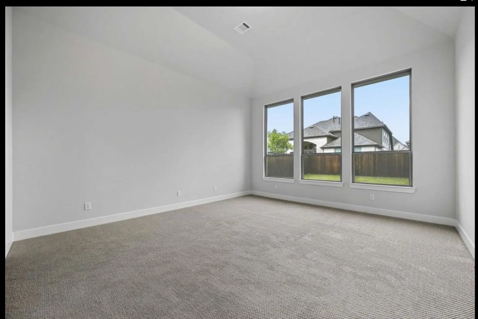 Vaulted ceiling, three large rectangular windows, neutral-toned carpeting, and light-colored walls