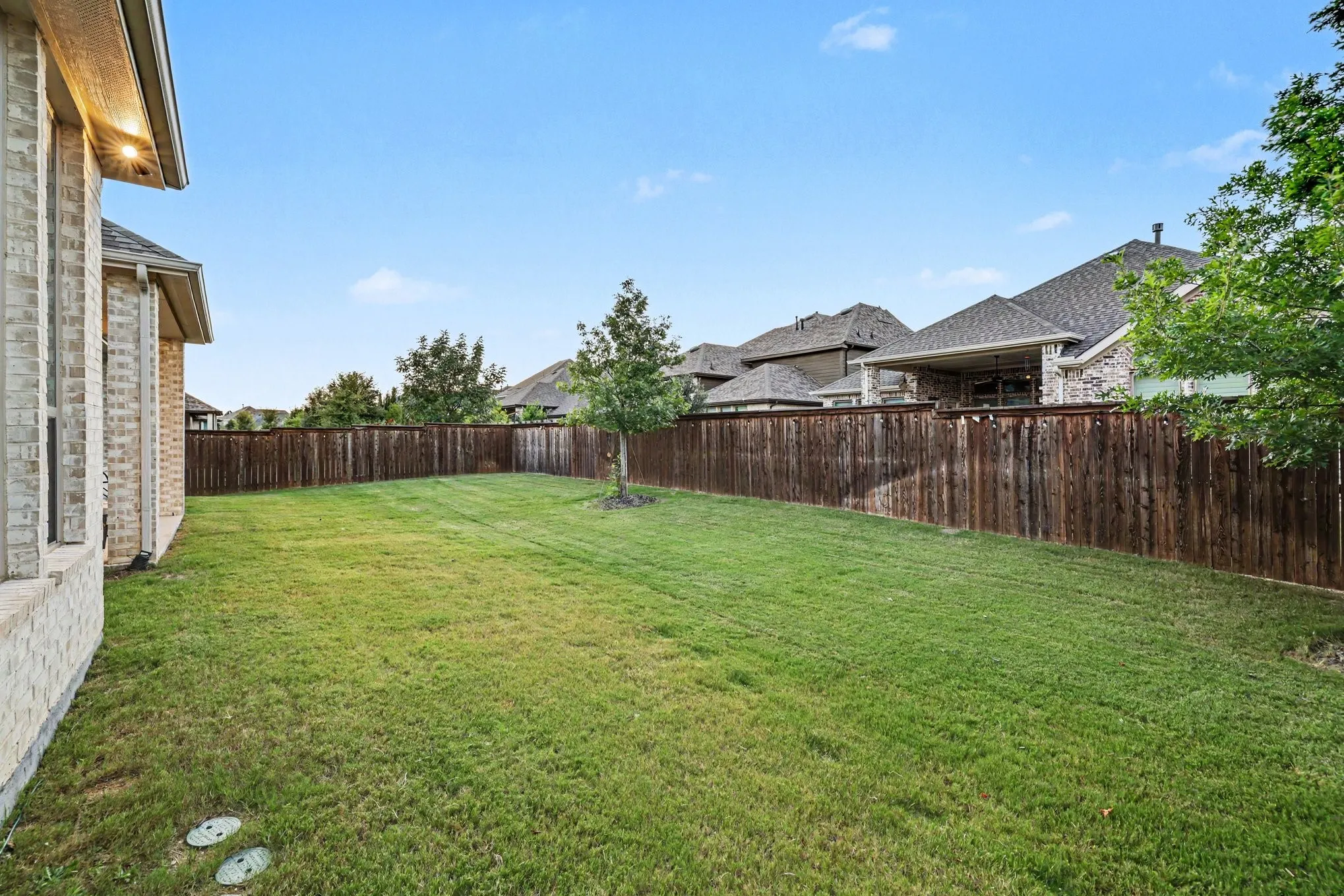 Expansive backyard featuring a manicured lawn, established privacy fencing, and a mature tree