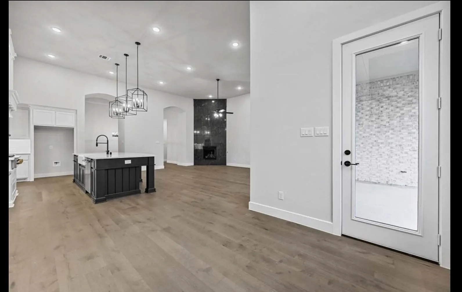 Wood-finish flooring throughout, kitchen island with built-in sink and three hanging light fixtures, recessed lighting, and a dark stone-clad fireplace
