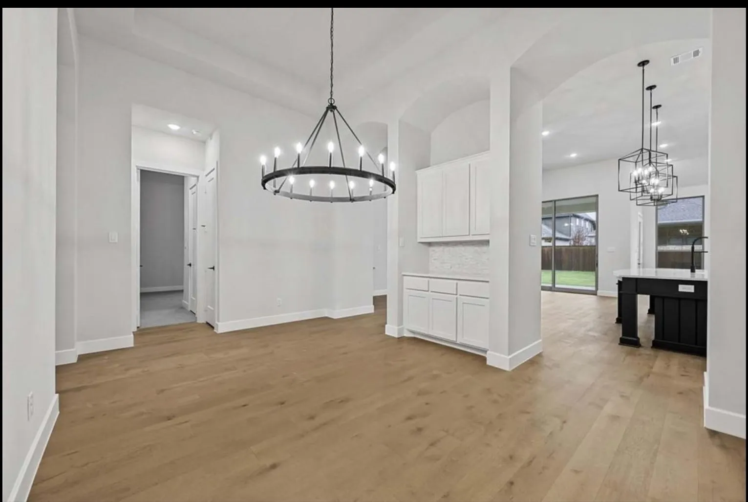 Wide-plank wood-finish flooring, white cabinetry, light-colored backsplash, modern overhead lighting, and arched doorways