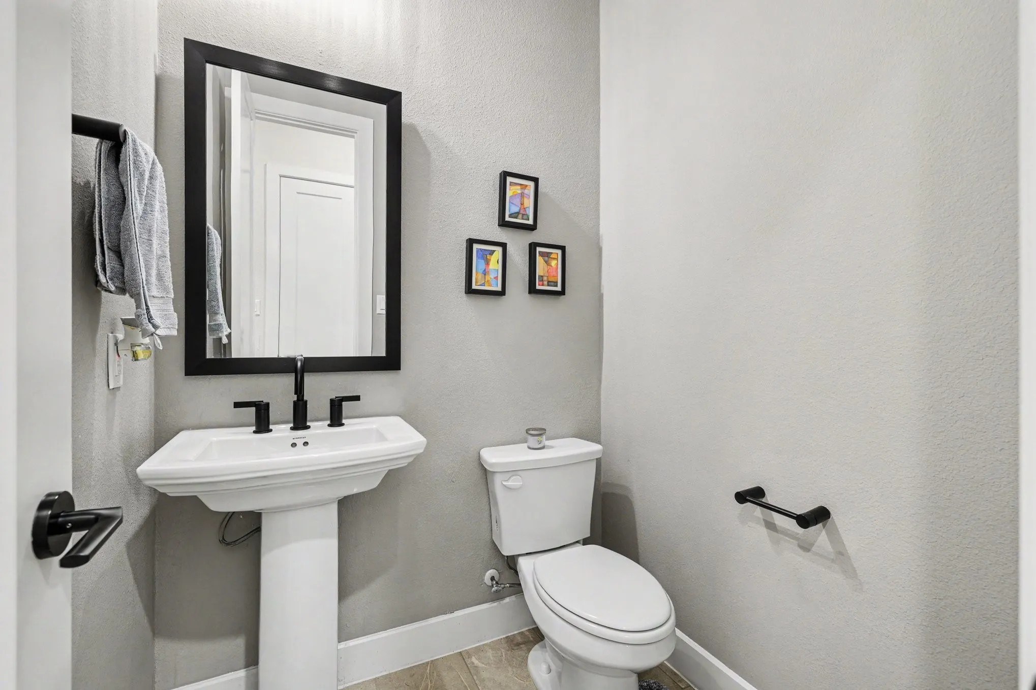 Pedestal sink with a black-framed mirror, matte black faucet, and coordinating toilet