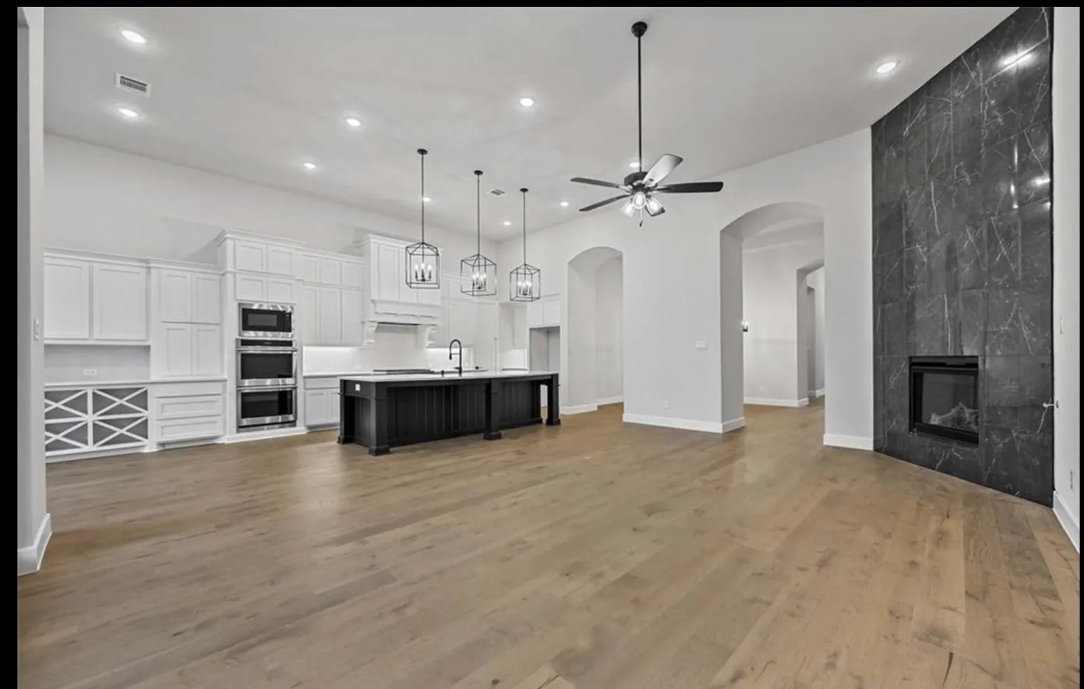 Open-concept living area featuring wood-finish flooring, a contemporary fireplace with a stone-look surround, an expansive kitchen island with pendant lighting, and recessed lighting throughout