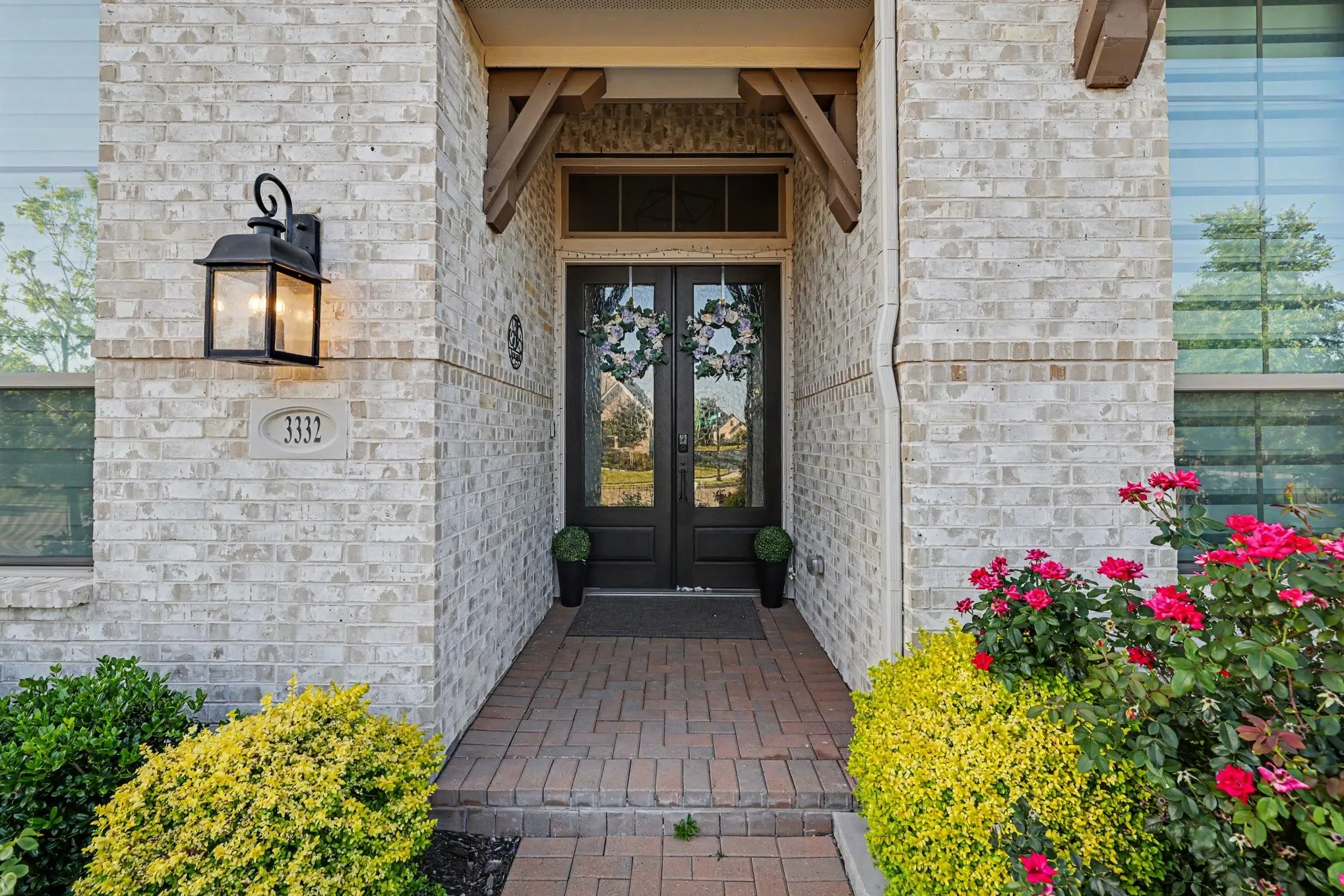 Light-colored brick exterior featuring a paver walkway, double entry doors with glass panels, and a prominent exterior light fixture