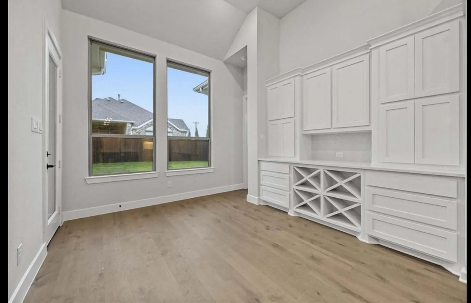 Wood-finish flooring, built-in white cabinetry, integrated wine storage, and large windows