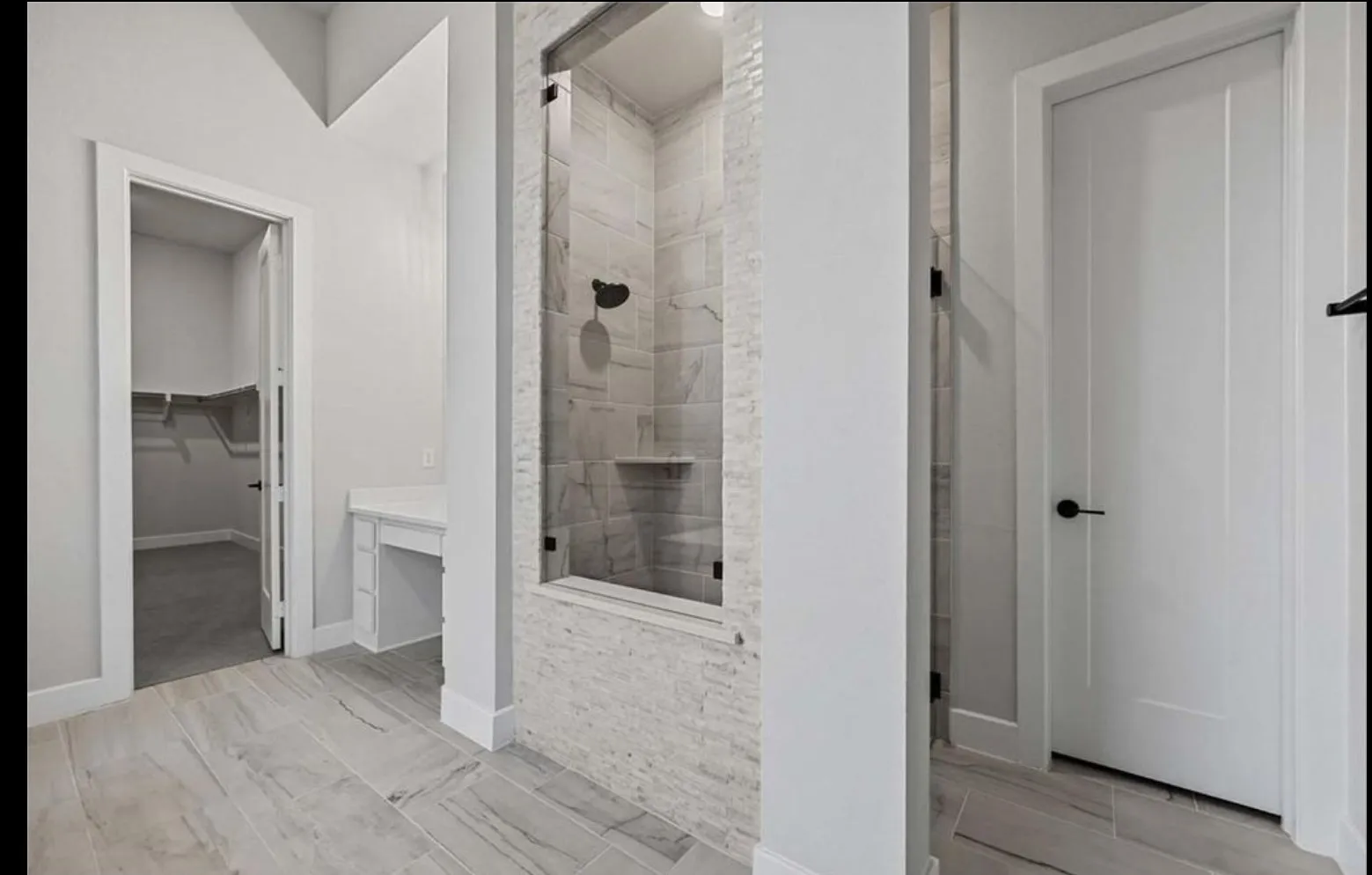 Glass-enclosed shower with tile surround and integrated shelving, featuring a built-in vanity, and wood-finish flooring