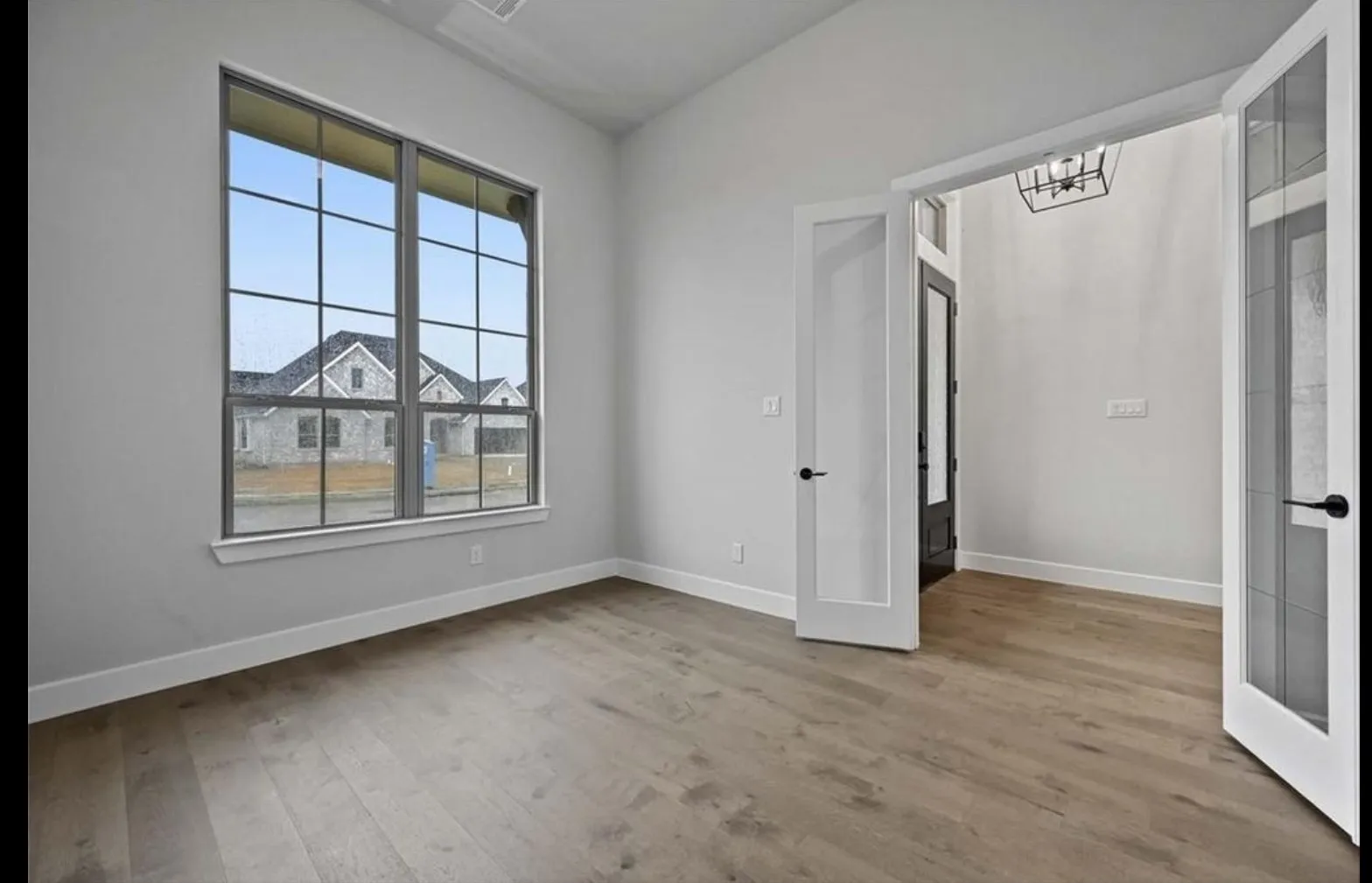 Wood-finish flooring, high ceilings, large window with grid pattern, and double French doors with frosted glass panels