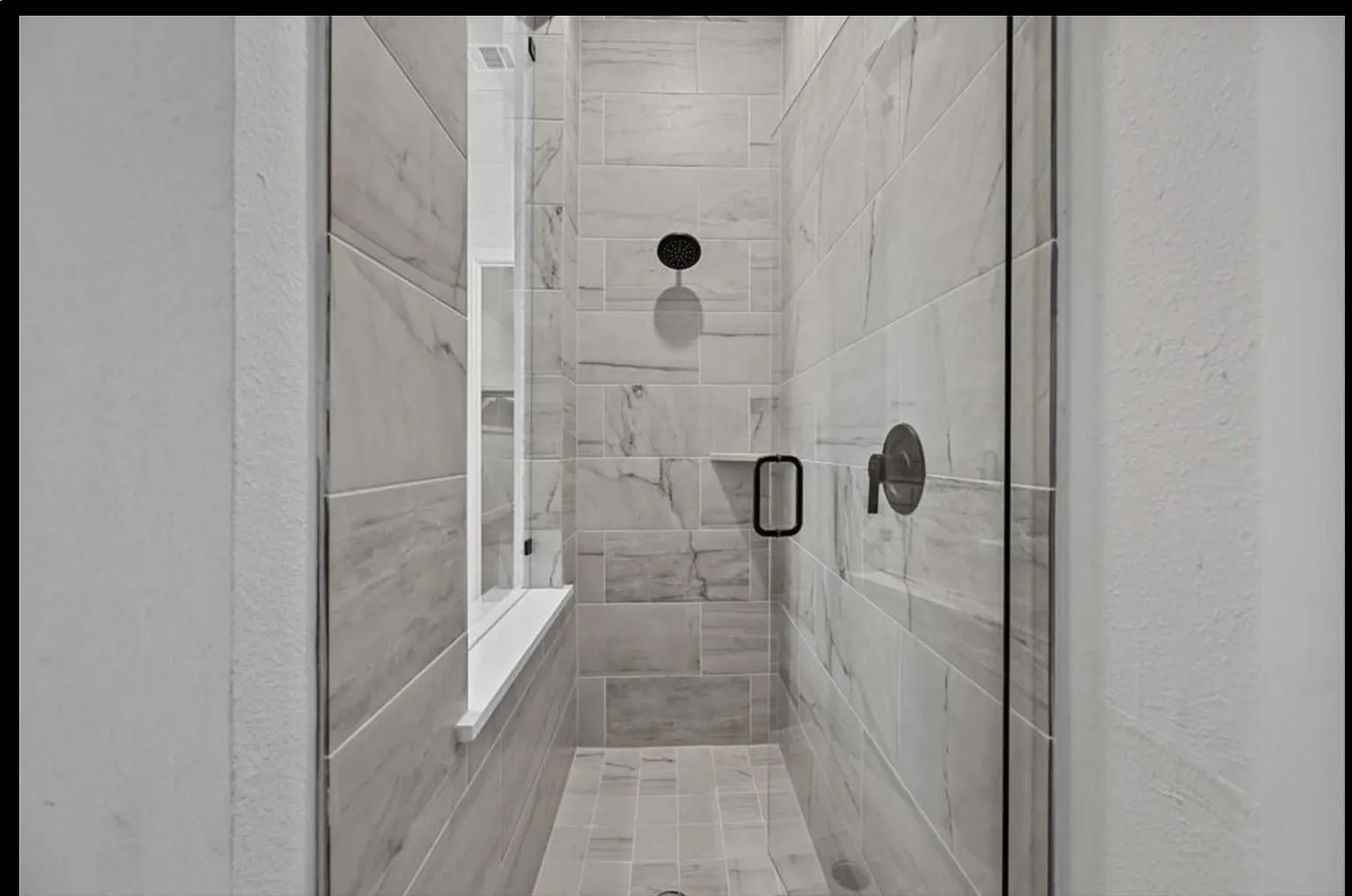 Walk-in shower featuring light-toned tile, a glass enclosure, and matte black fixtures