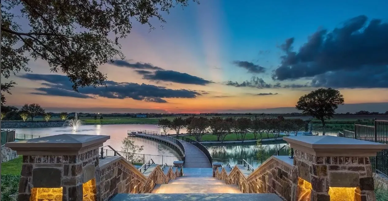 Stone-clad staircase with recessed lighting leading to a waterfront area featuring a fountain, a curved pier, and mature trees