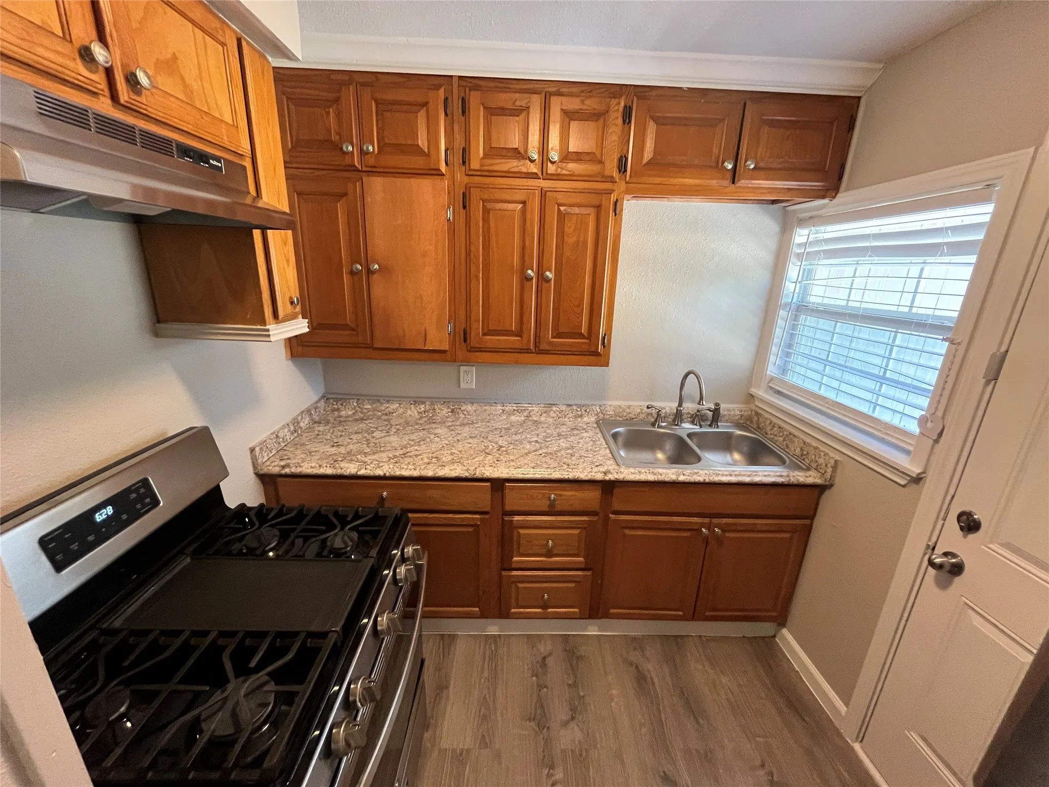 Wood-finish flooring, stainless steel range with griddle, wood cabinetry, dual basin stainless steel sink, and light-toned countertops