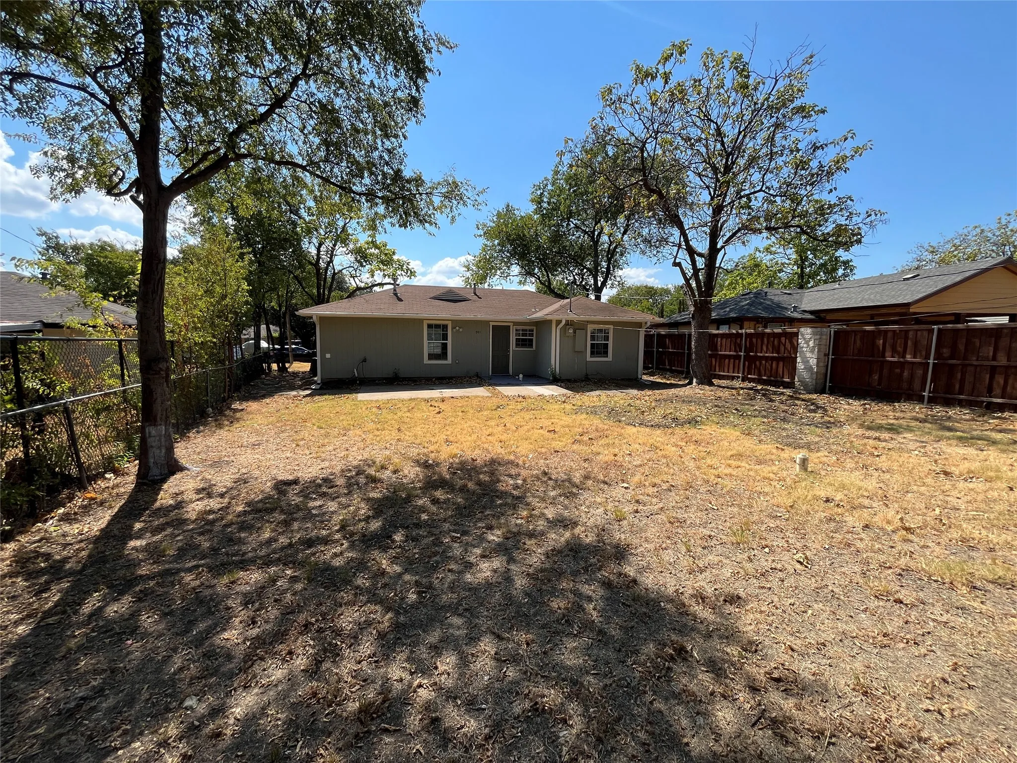 Expansive backyard with a concrete patio, mature trees, and a combination of chain-link and wood privacy fencing