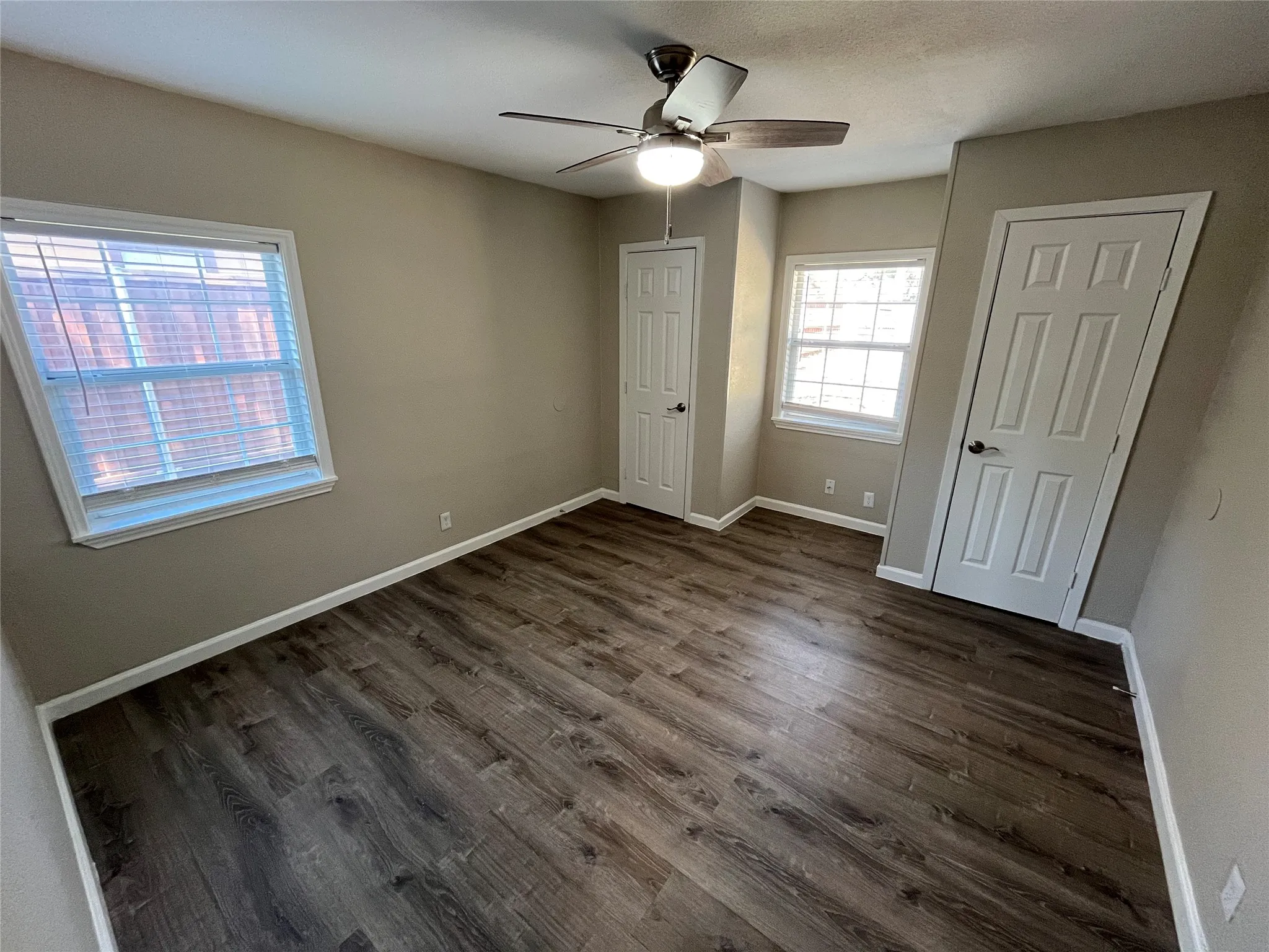 Wood-finish flooring, light tan wall color, white trim, two panel doors, and a ceiling fan with integrated lighting