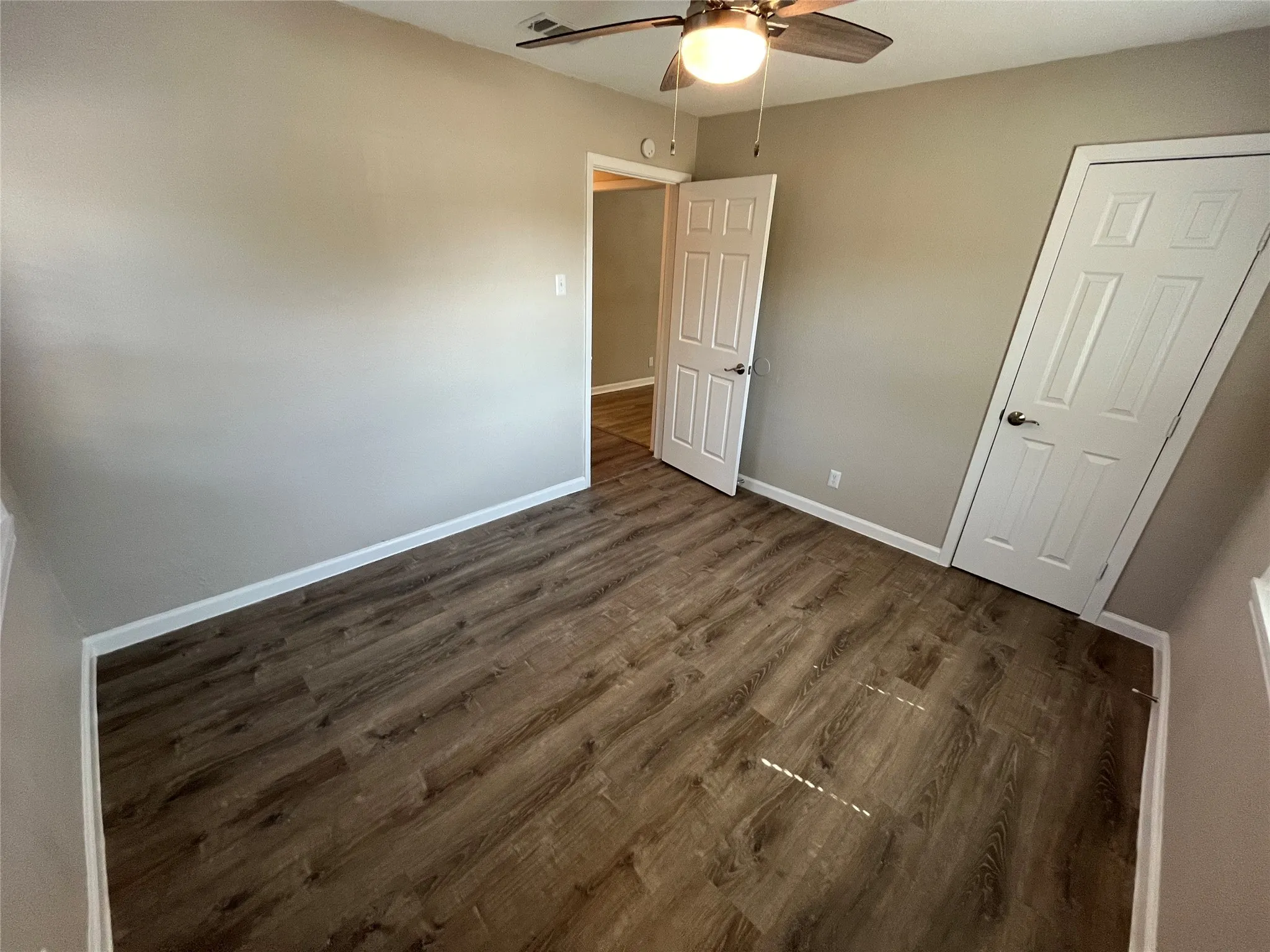 Wood-finish flooring, neutral wall tones, and a ceiling fan with integrated lighting