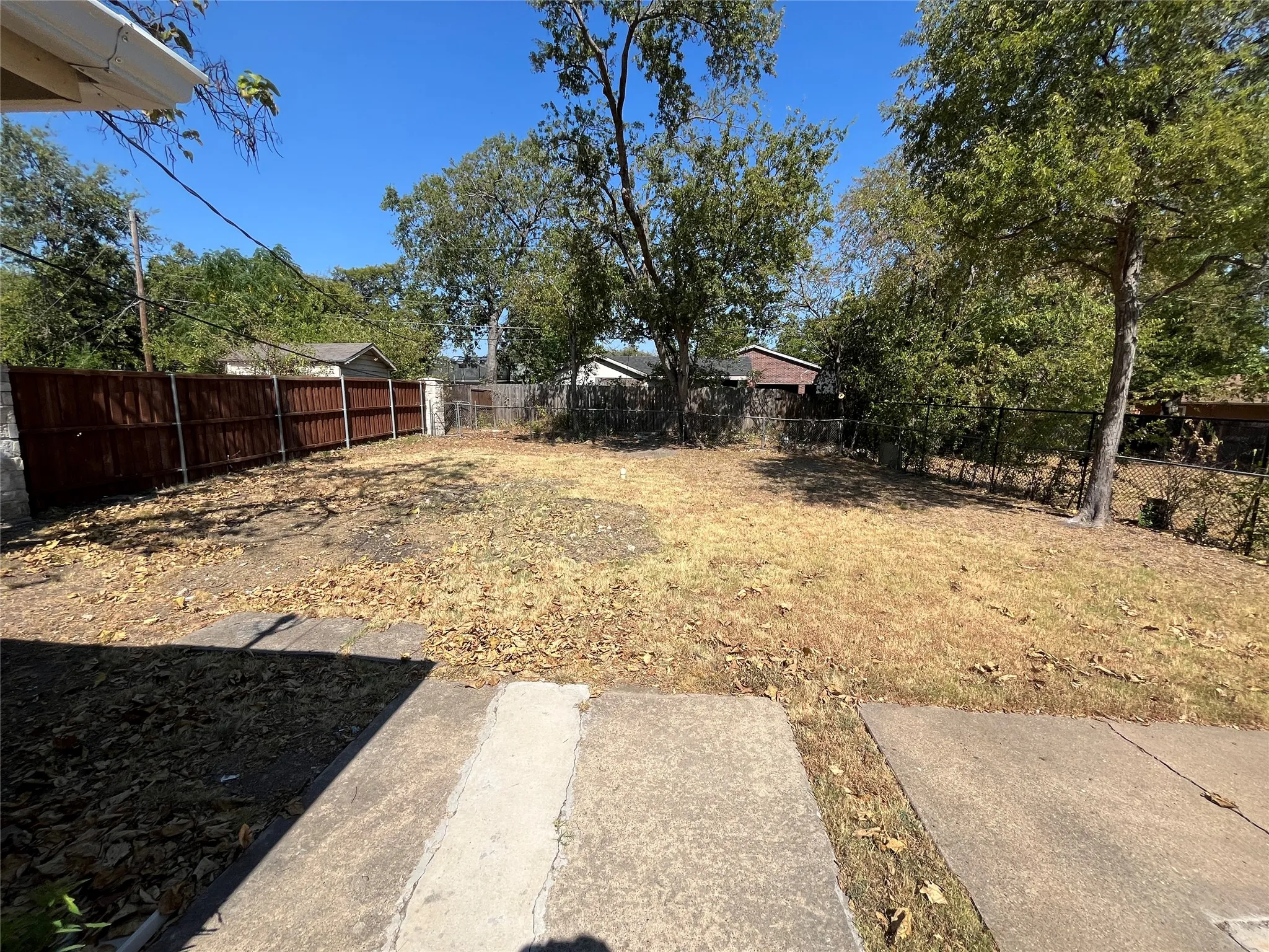 Expansive outdoor area with a wood privacy fence, mature trees, and concrete patio sections