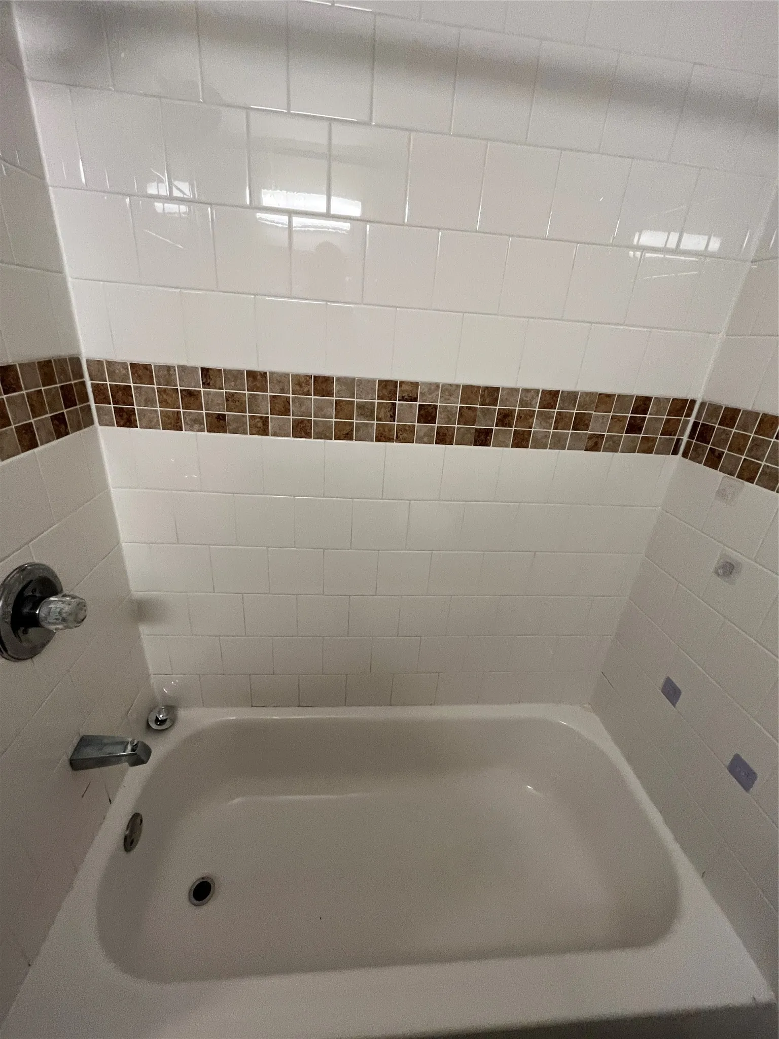 White tiled shower surround with an accent mosaic band