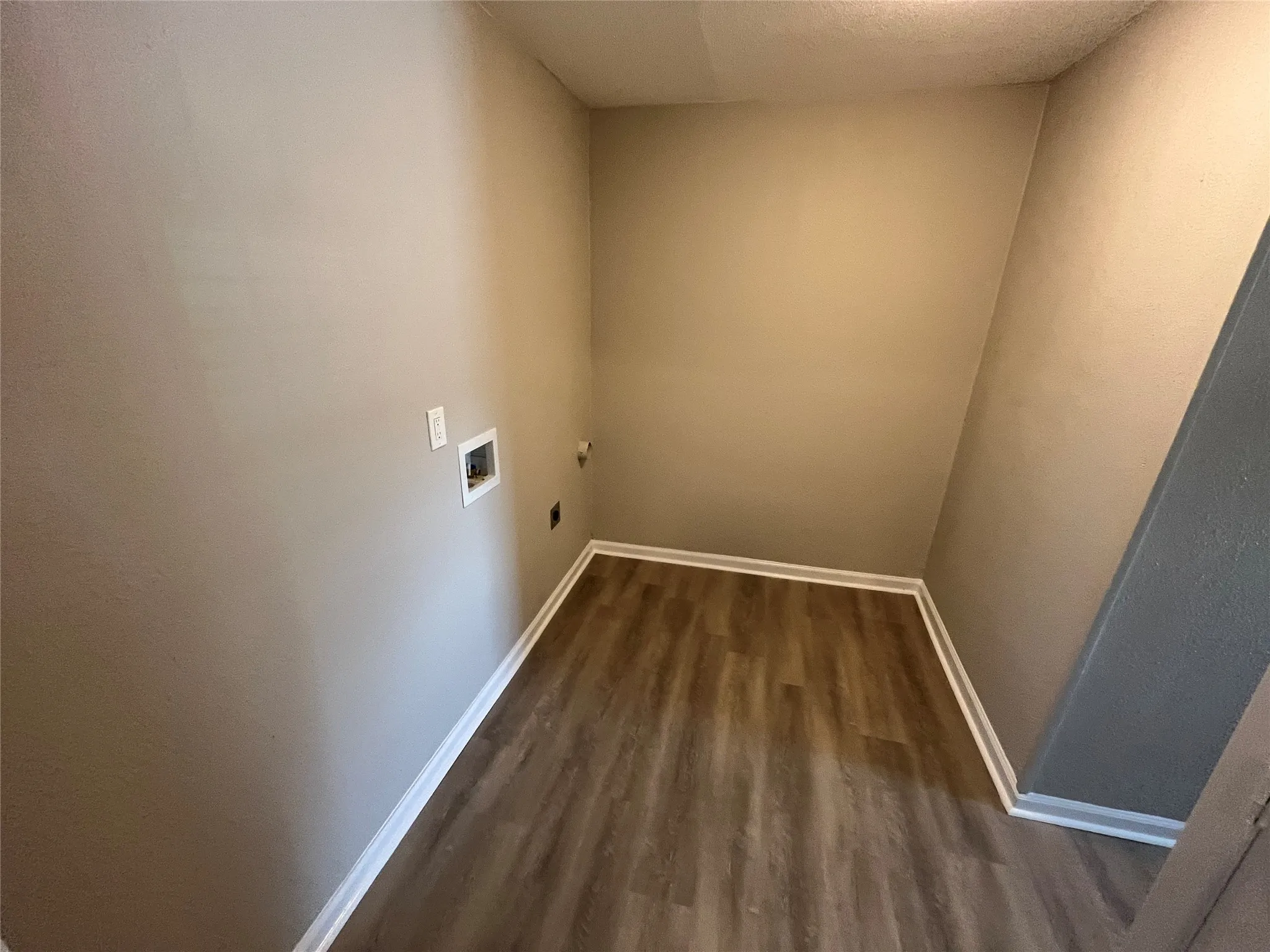 Wood-finish flooring with white baseboards, neutral wall color, and visible utility connections