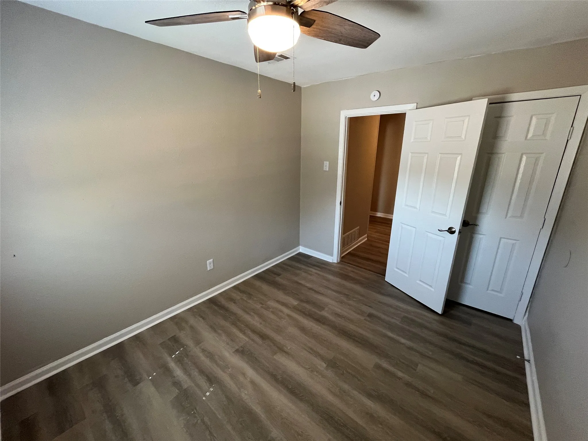 Wood-finish flooring, neutral wall paint, ceiling fan with integrated lighting, and white paneled doors
