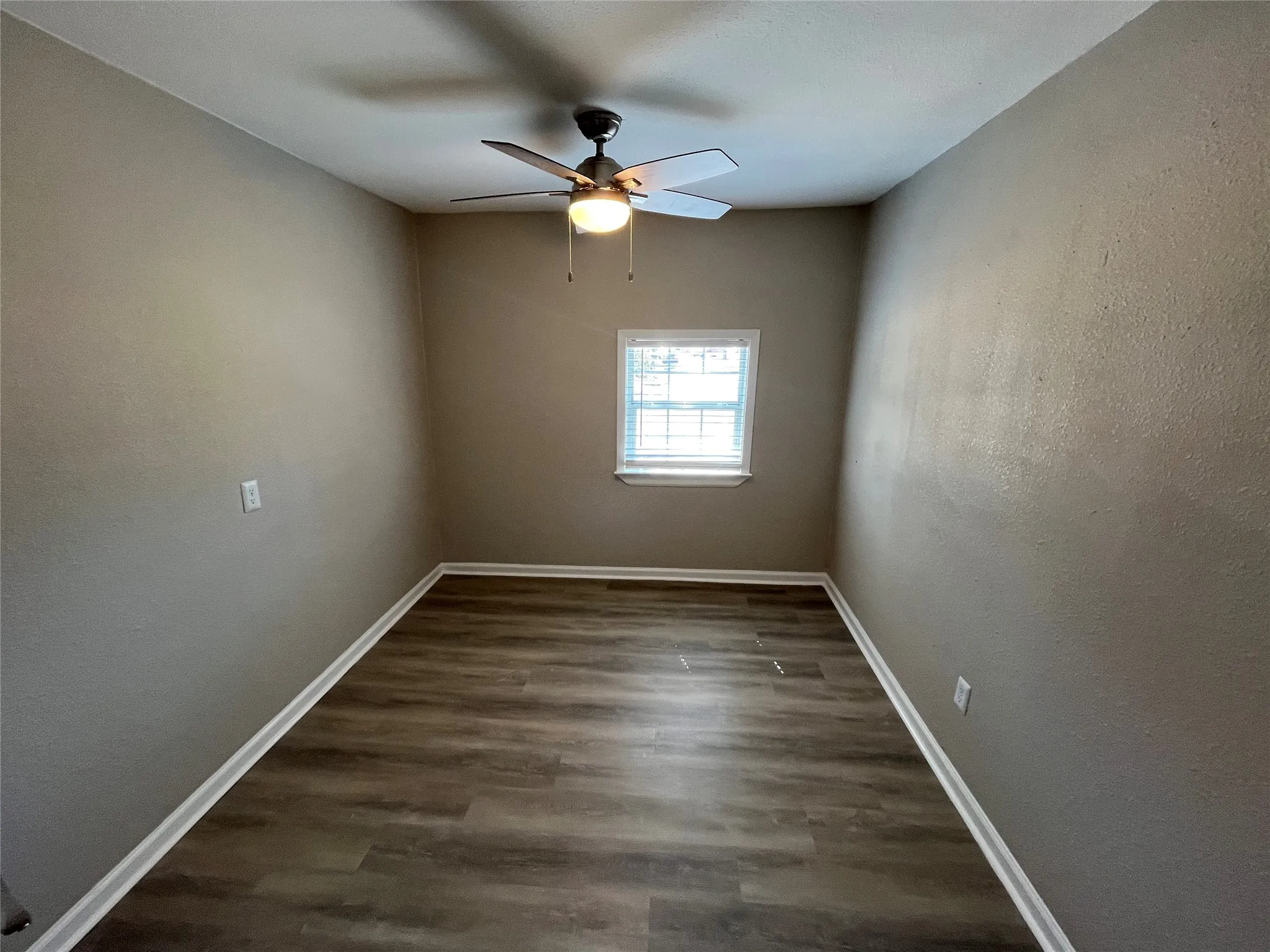 Wood-finish flooring, single window with blinds, ceiling-mounted fan with integrated lighting, and neutral wall tones