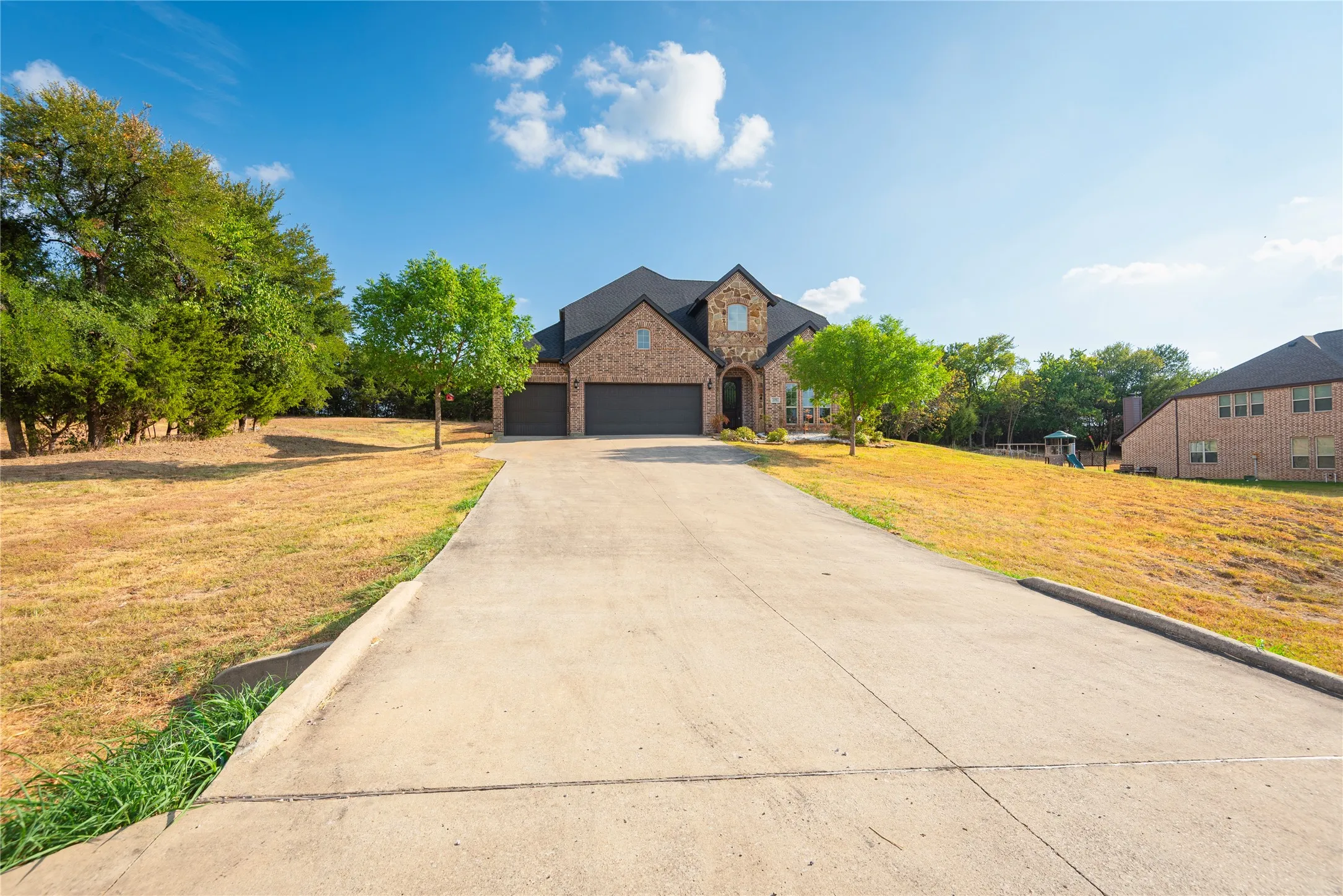 Brick exterior with stone accents, dark-toned roof, attached garage, and a concrete driveway..more acreage to the left