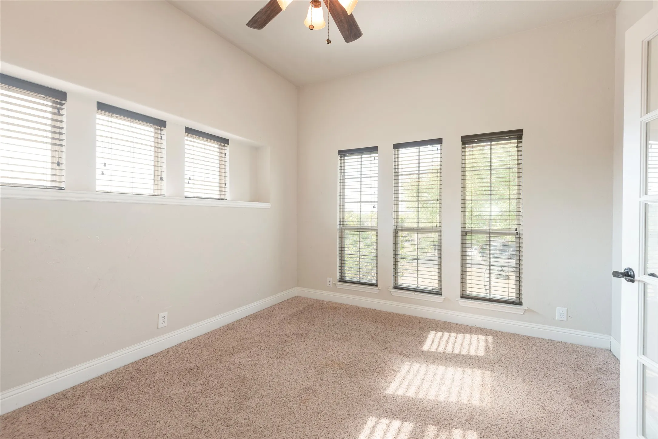 Office-Vaulted ceiling with a ceiling fan, three tall windows with blinds, three transom windows with blinds, and light-colored carpeting