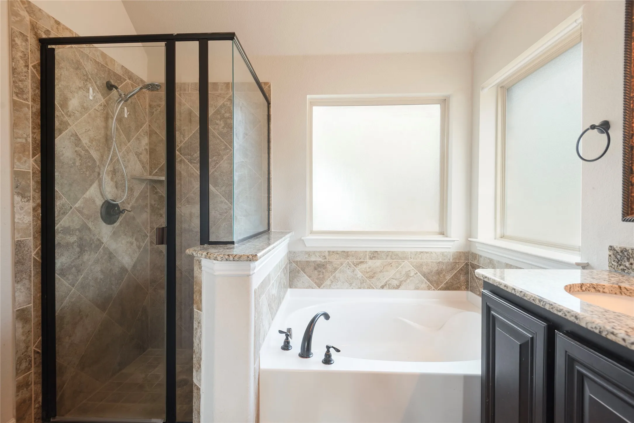 Walk-in shower with tiled surround, separate soaking tub, granite countertops, dark wood-finish cabinetry, and frosted windows