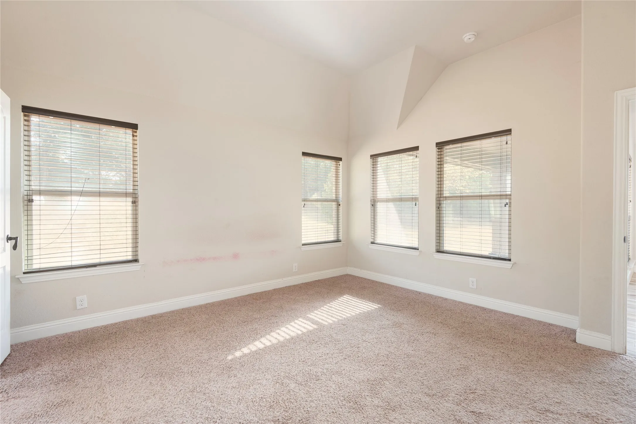 Primary bedroom 1st floor Vaulted ceiling, multiple windows with blinds, light-colored carpet flooring, and neutral wall tones
