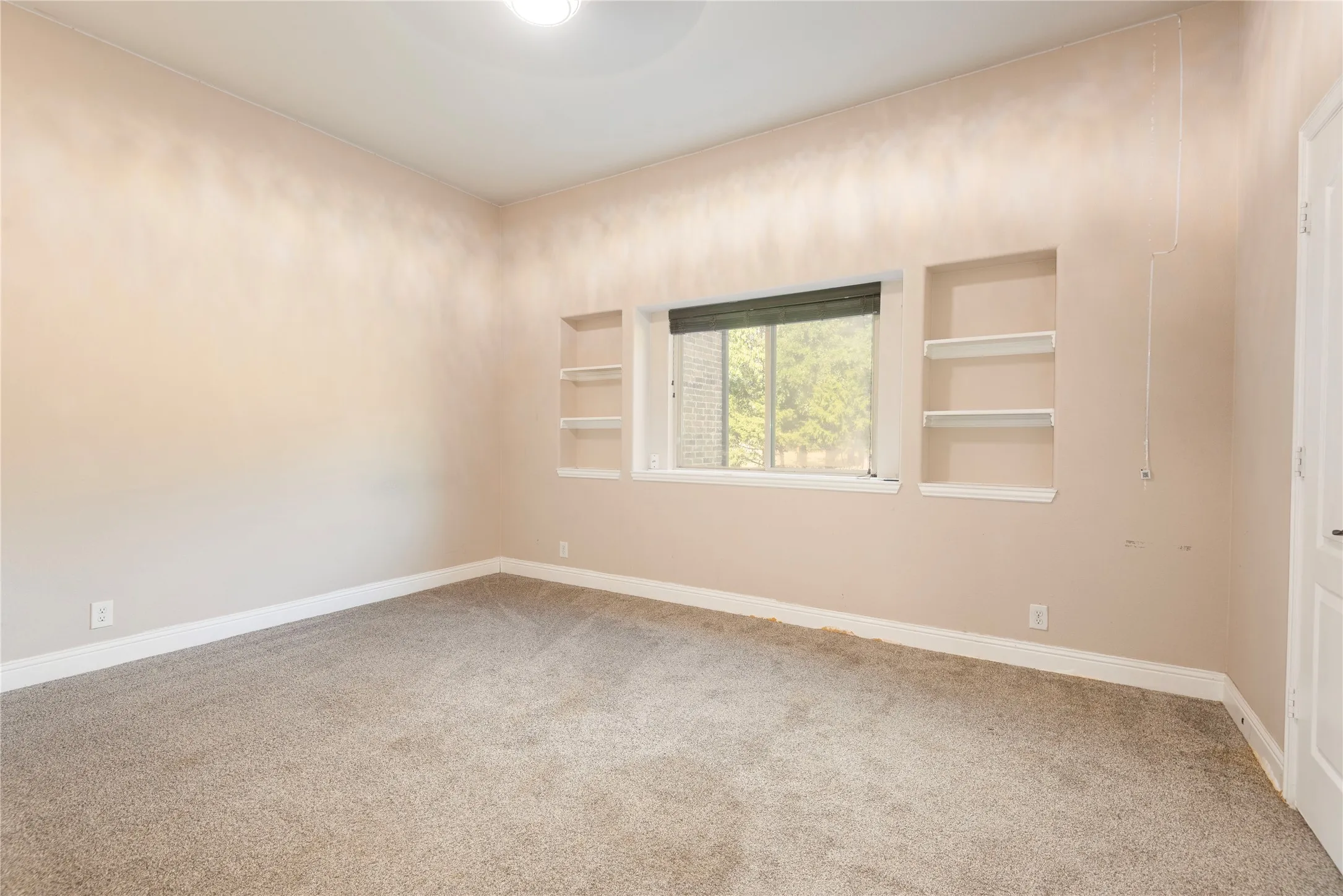 2nd downstairs bedroom Recessed shelving, wall-to-wall carpeting, and a window with blinds provide functional elements