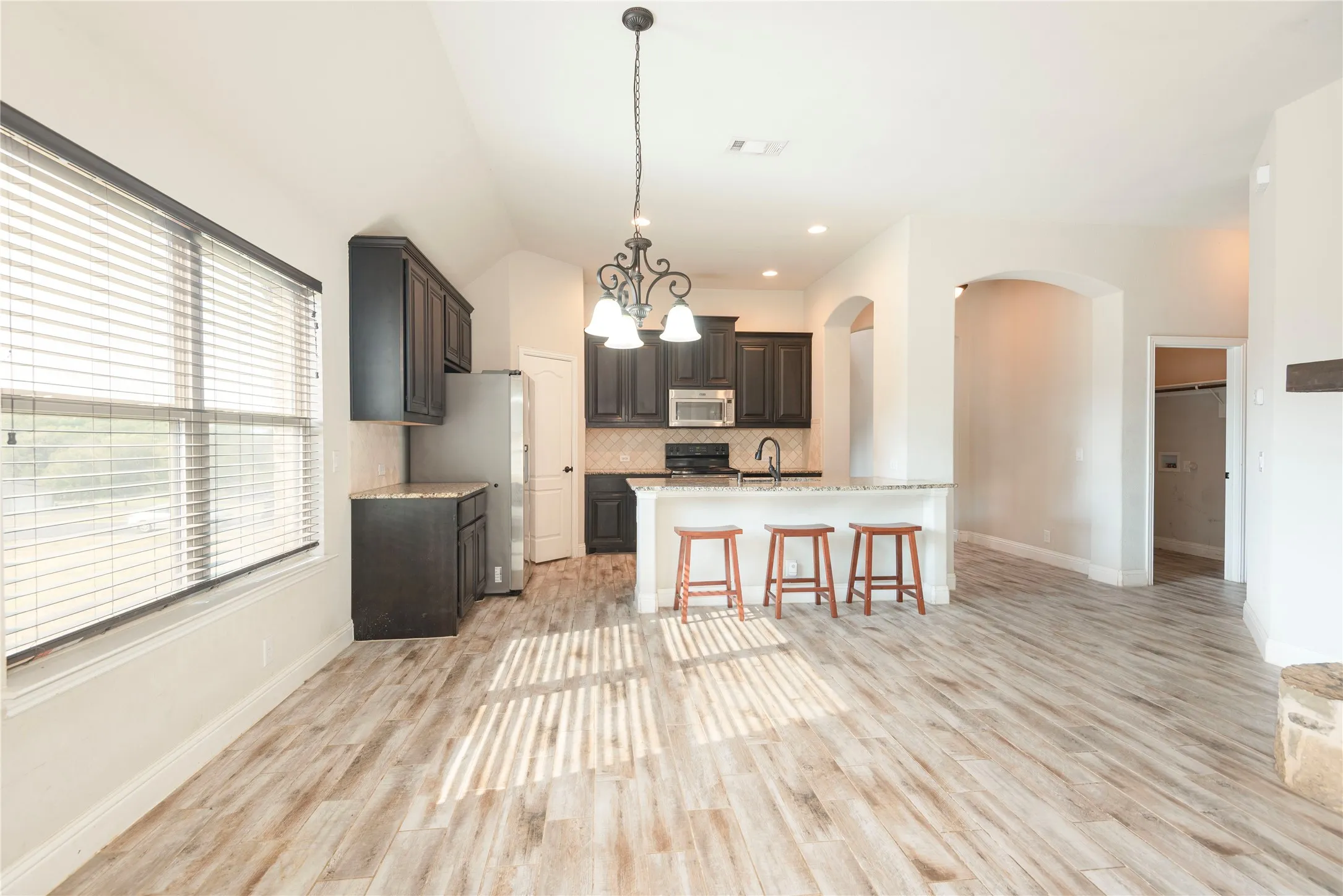 Vaulted ceiling with decorative chandelier, tile flooring, dark wood-finish cabinetry,  with integrated sink, and stainless steel appliances