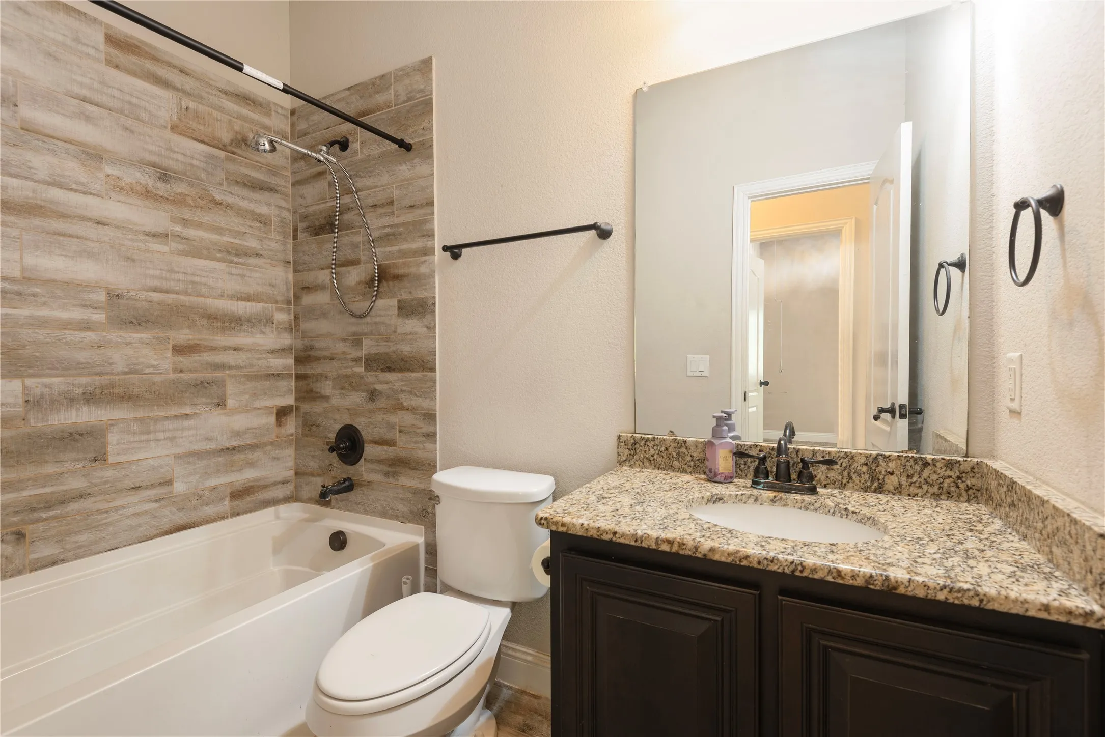 Downstairs Guest Bathroom with Bathtub with wood-look tile surround, dark wood-finish vanity with granite countertop, integrated sink, and dark bronze fixtures