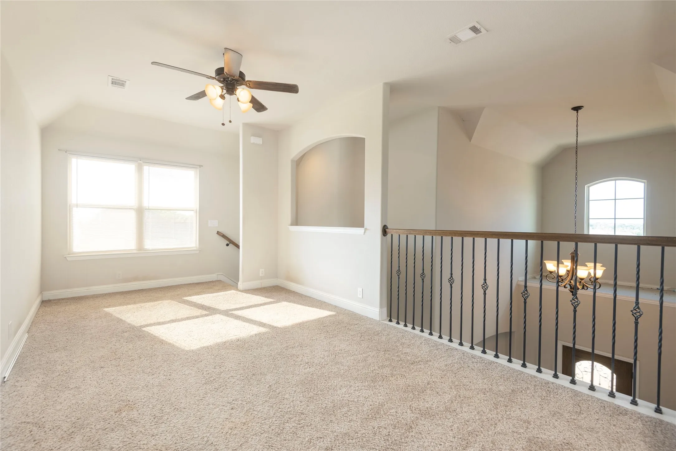 Carpeted loft area featuring a ceiling fan with integrated lighting, a double window, and a wrought iron and wood-finish railing overlooking the lower level