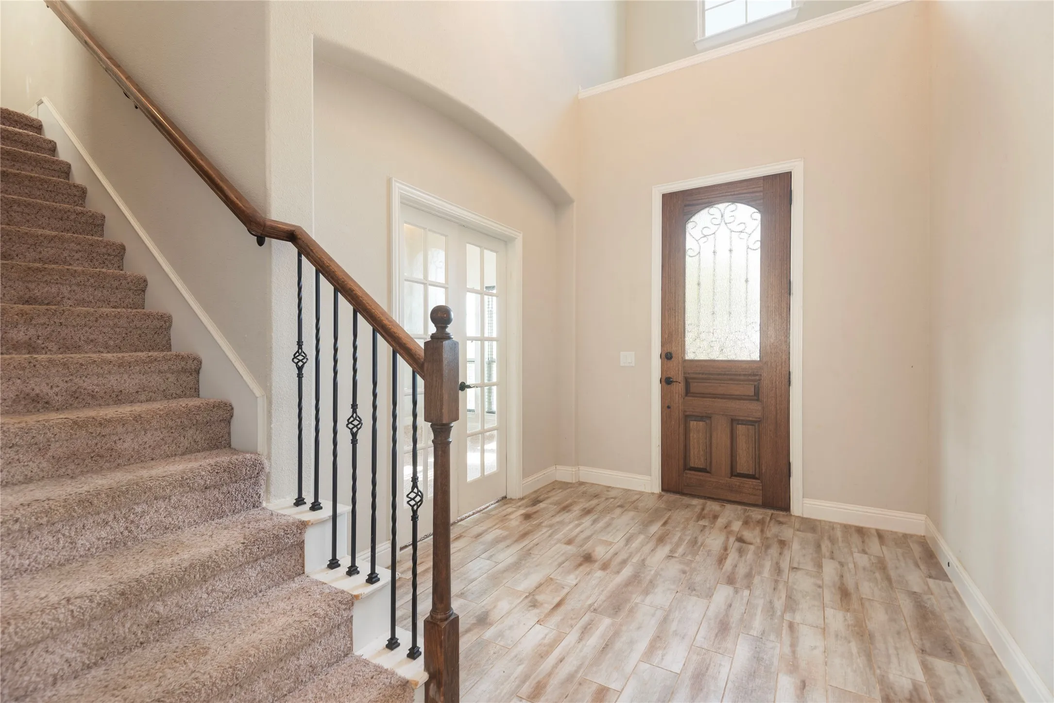 Wood-look tile  flooring, staircase with wrought iron balusters, and a solid wood entry door with decorative glass