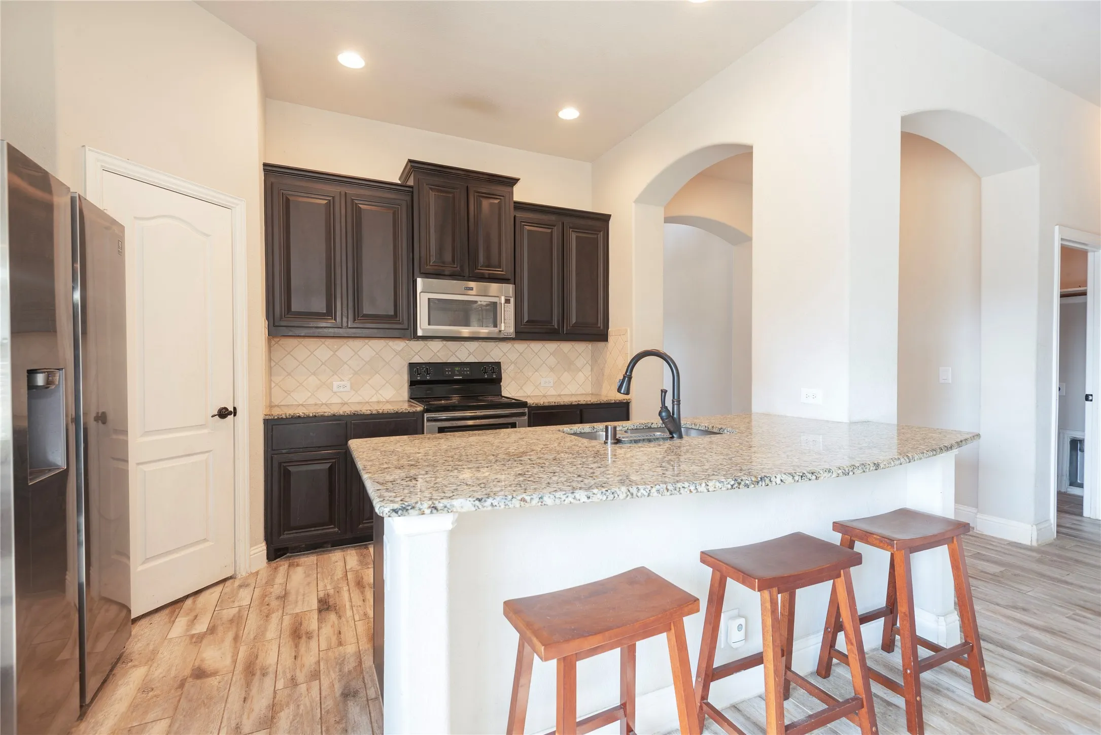 Kitchen featuring, dark wood cabinetry, stainless steel appliances, and a curved island with a light-toned countertop