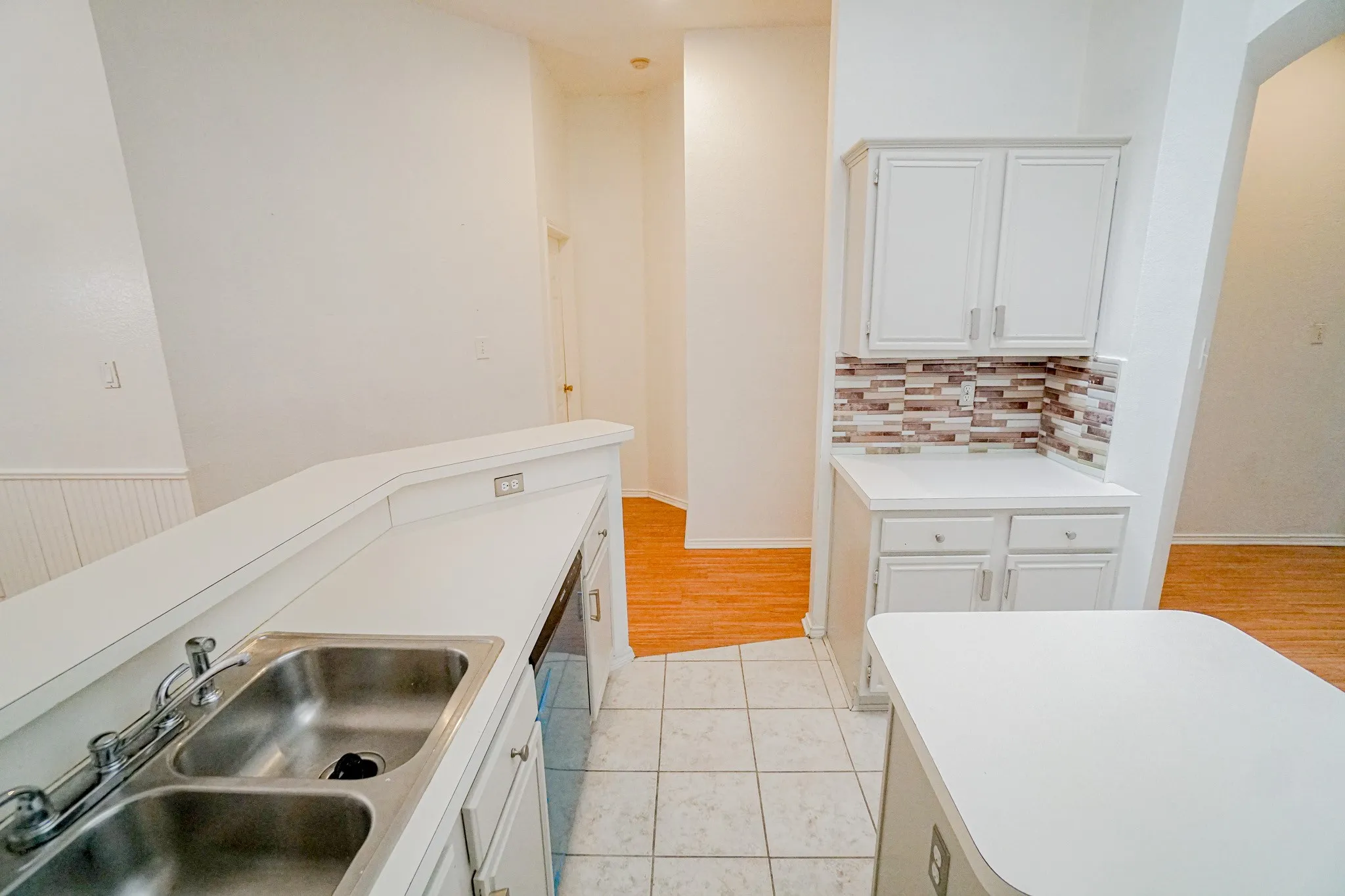 Kitchen featuring white cabinetry, dual basin stainless steel sink, white countertops, and a mosaic tile backsplash