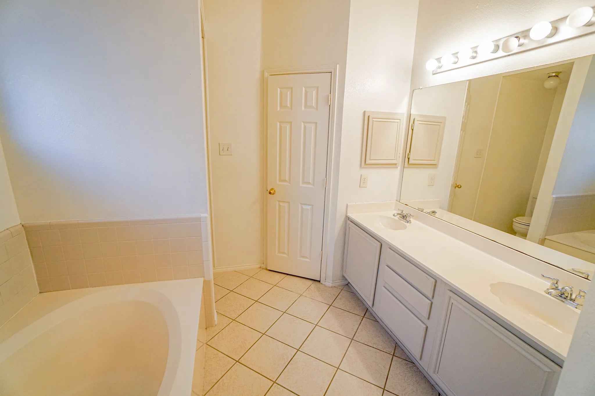 Bathroom featuring a dual vanity, large mirror, recessed medicine cabinets, tile flooring, and a built-in tub