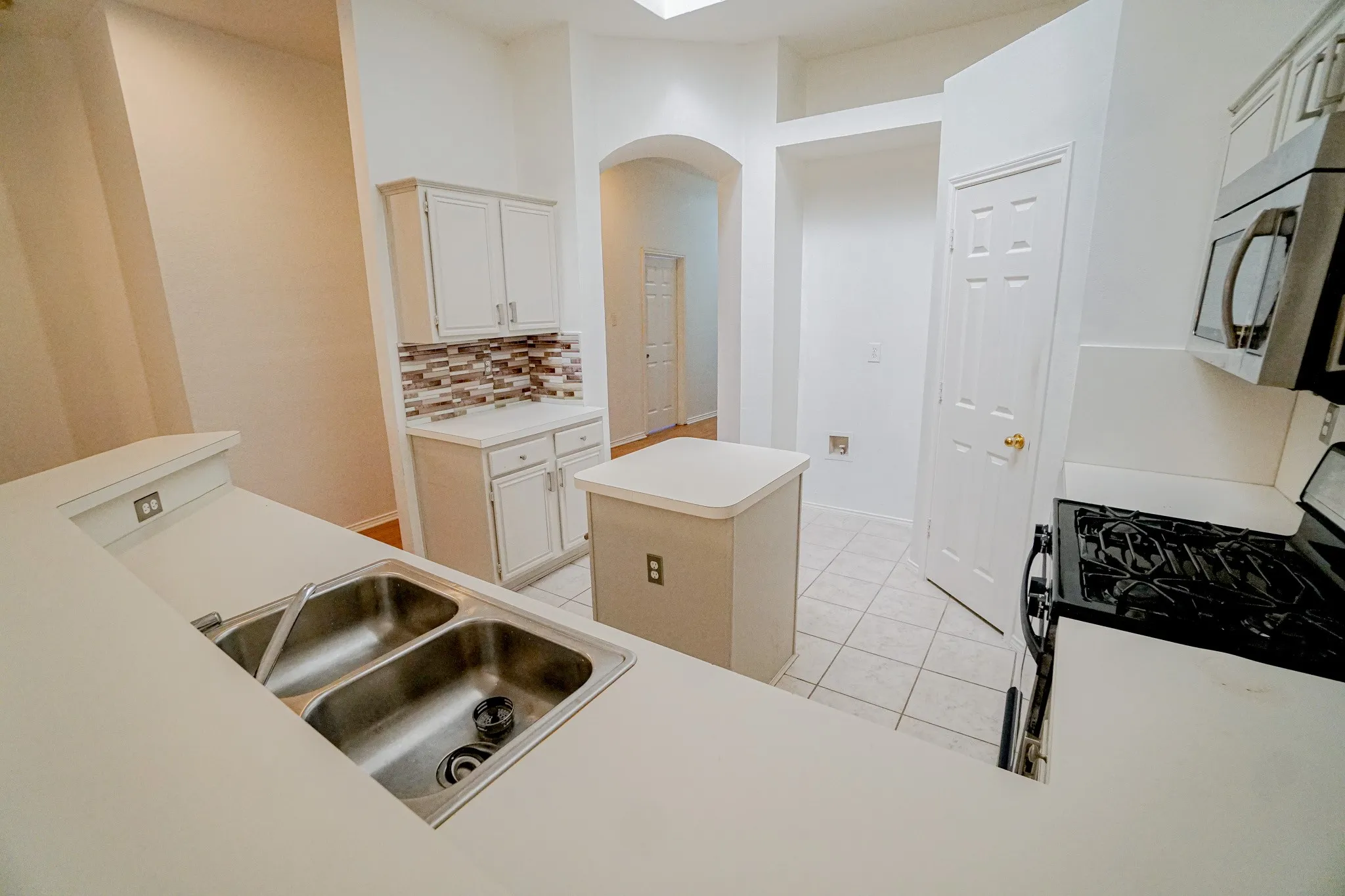 White cabinetry, stainless steel double basin sink, mosaic tile backsplash, black gas range, and a central kitchen island