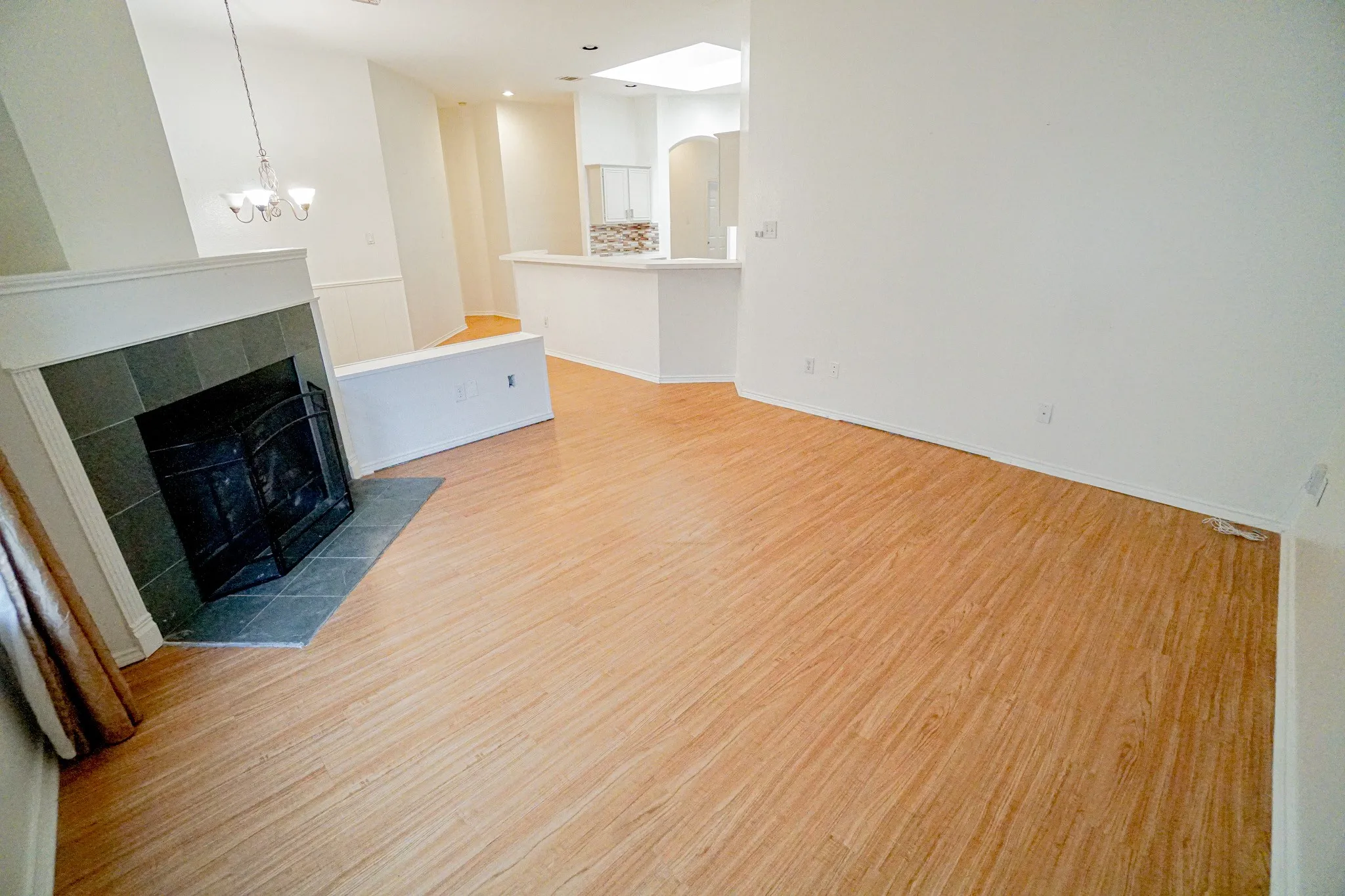 Wood-finish flooring throughout, tile-surround fireplace with a hearth, white walls, and a ceiling light fixture