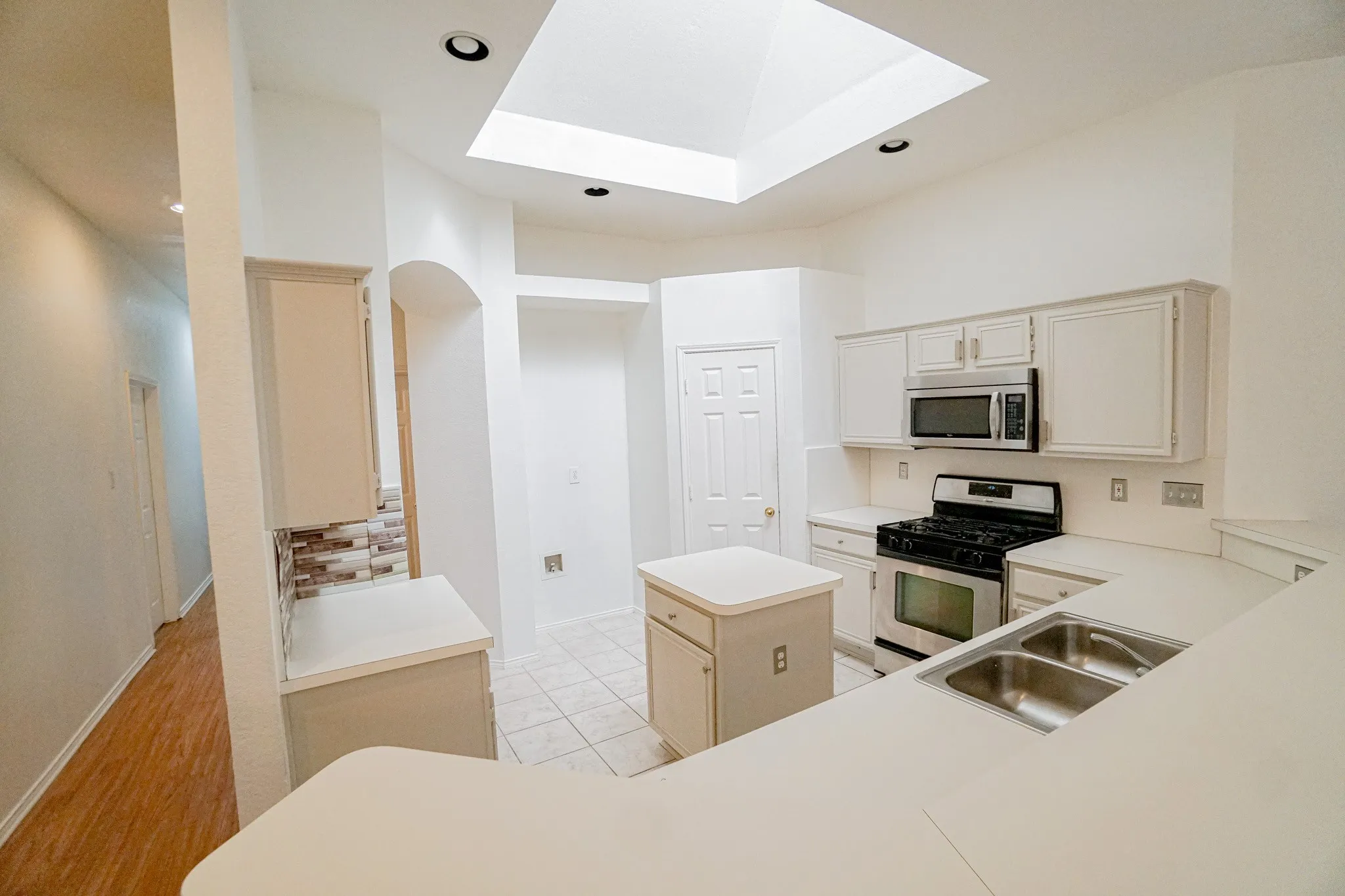 Kitchen view featuring a skylight, recessed lighting, white cabinetry, a double basin stainless steel sink, and a center island