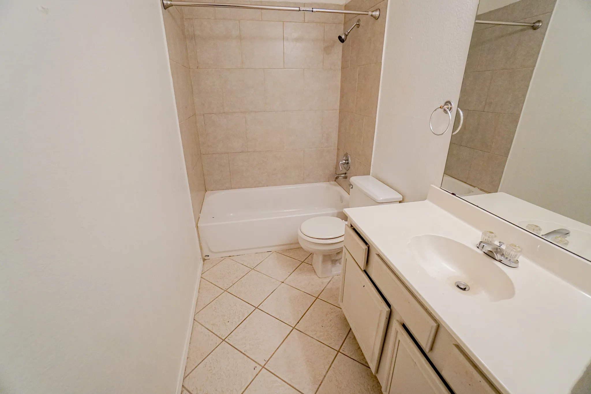 Bathroom featuring a white vanity with an integrated sink, a large mirror, a toilet, a bathtub, and tiled flooring