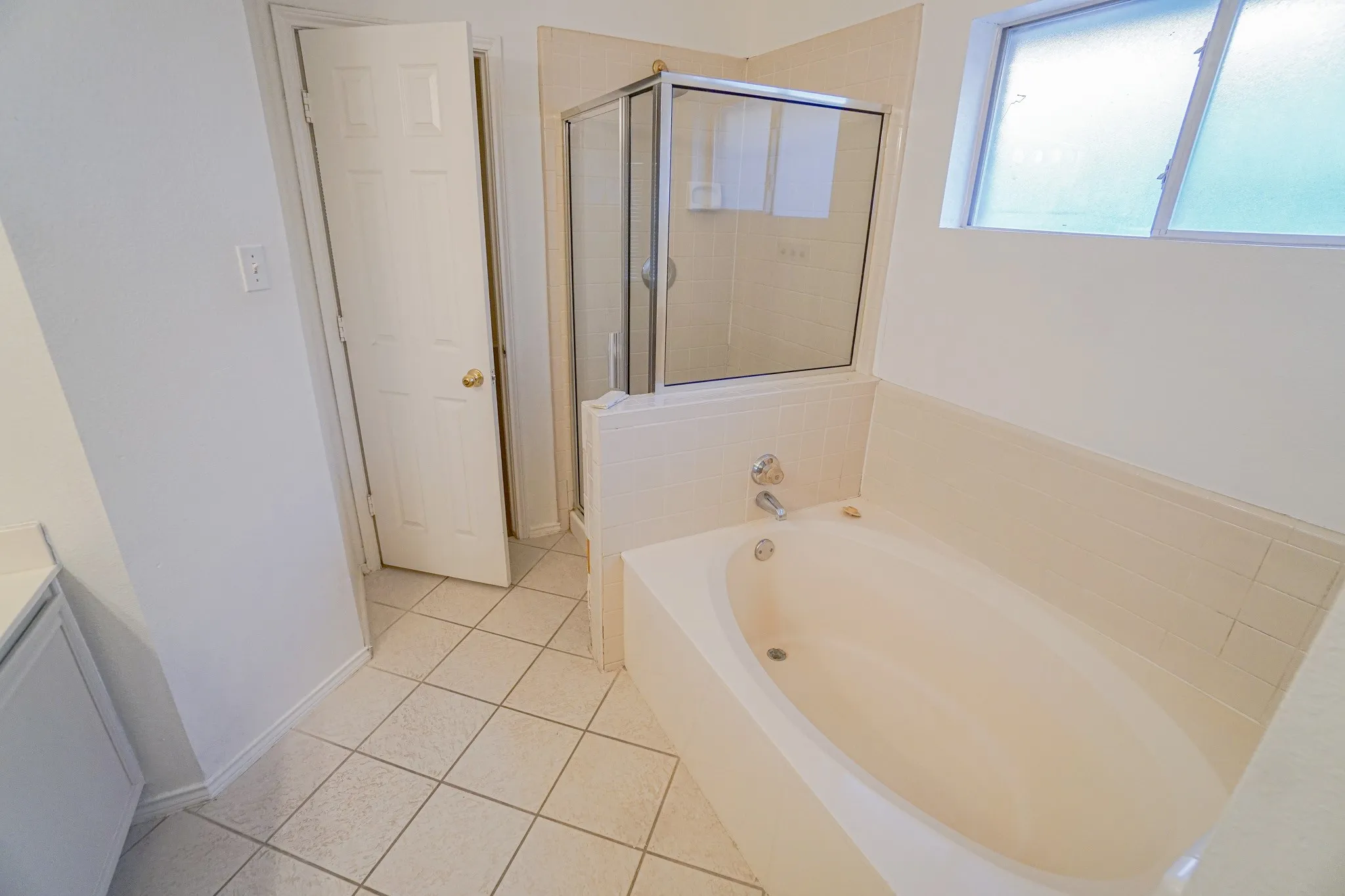 Soaking tub with chrome fixtures, tiled surround, glass-enclosed shower, and tiled flooring