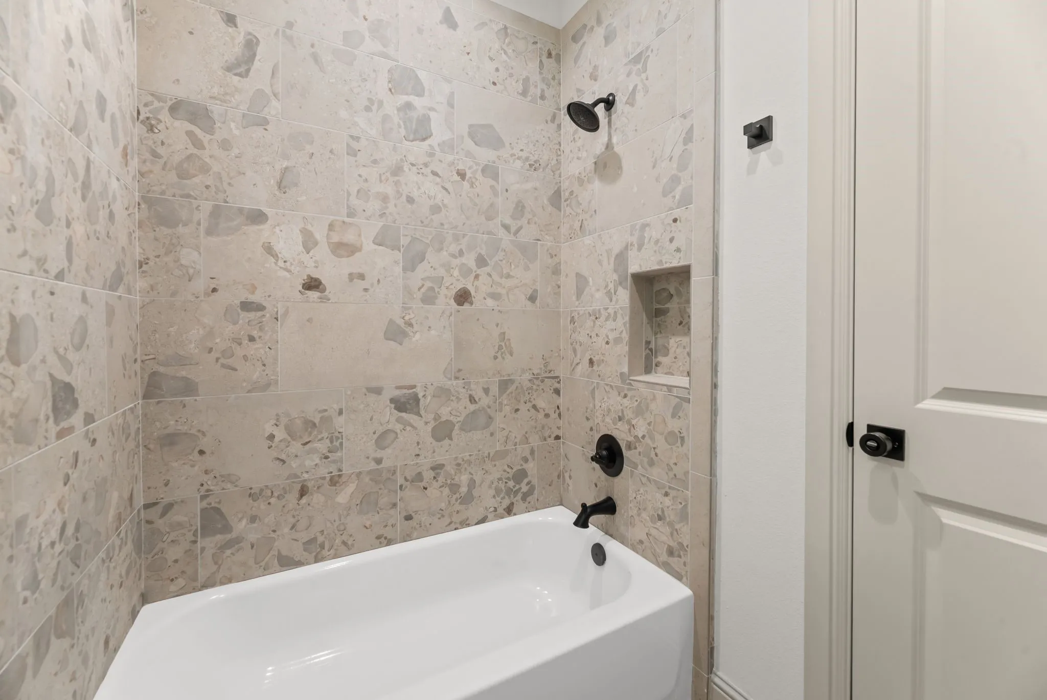 Secondary bath includes a tiled tub and shower combination with contemporary fixtures and timeless neutral finishes.