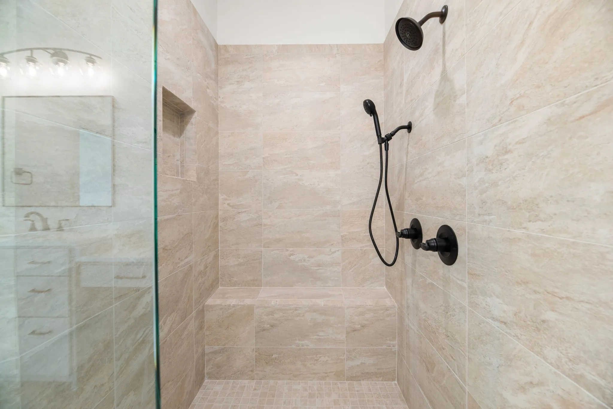Walk-in shower showcases beautiful tilework, glass enclosure, and contrasting dark fixtures in the home's sophisticated primary bathroom.