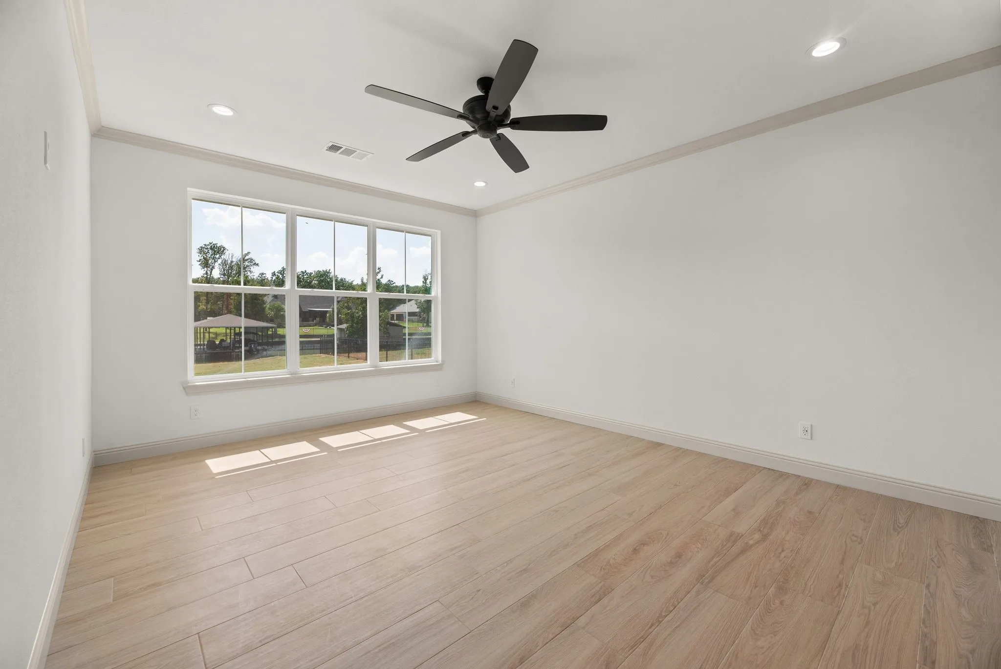 Spacious primary bedroom features abundant natural light, hard-surface flooring, a ceiling fan, and room for a comfortable private retreat.