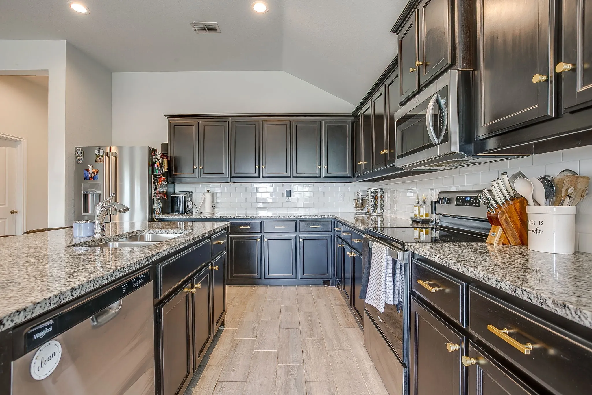 Kitchen featuring dark wood cabinetry with gold-tone hardware, granite countertops, subway tile backsplash, and stainless steel appliances