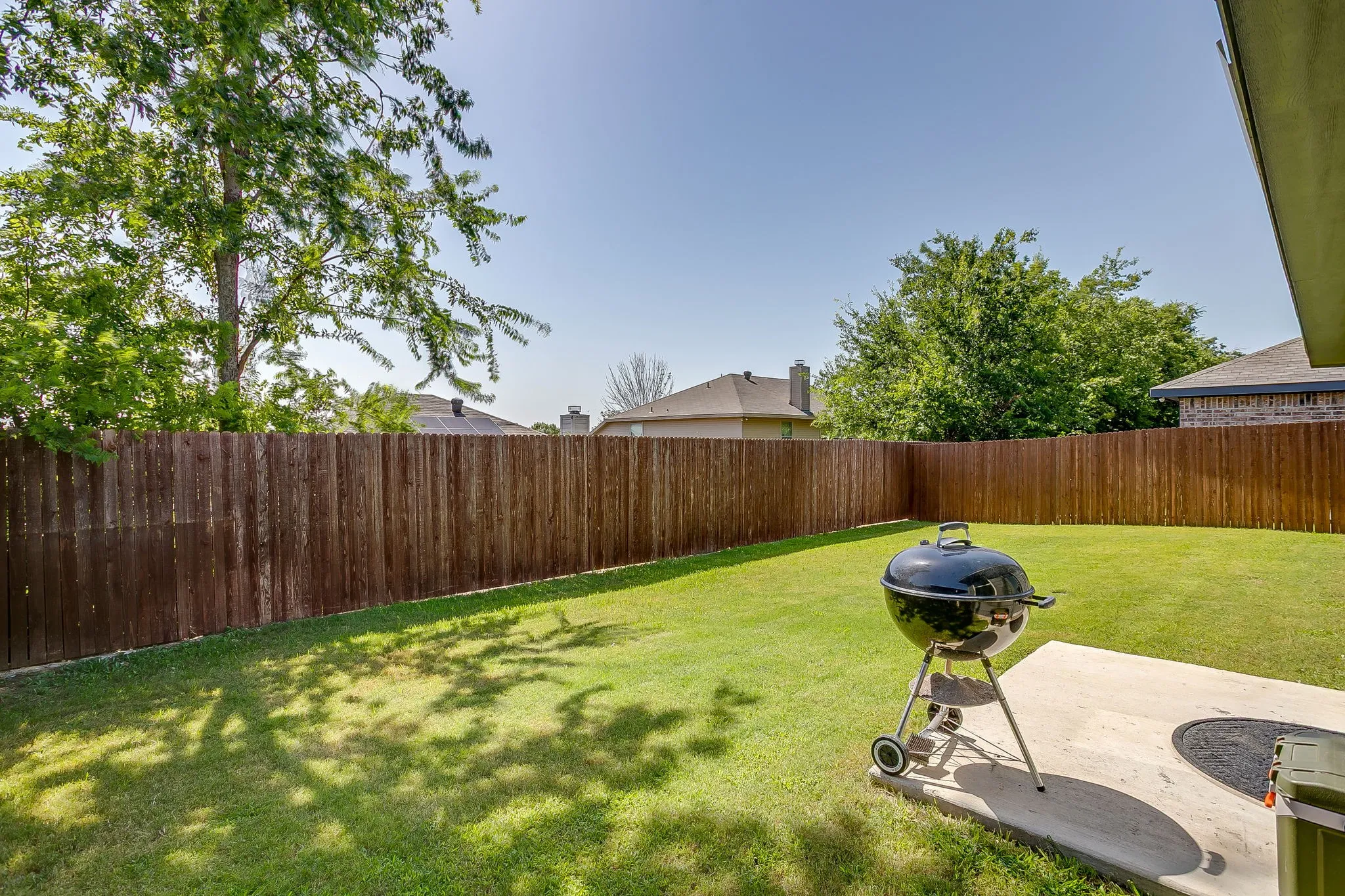 Expansive backyard featuring a manicured lawn, established trees, a wood privacy fence, and a concrete patio pad